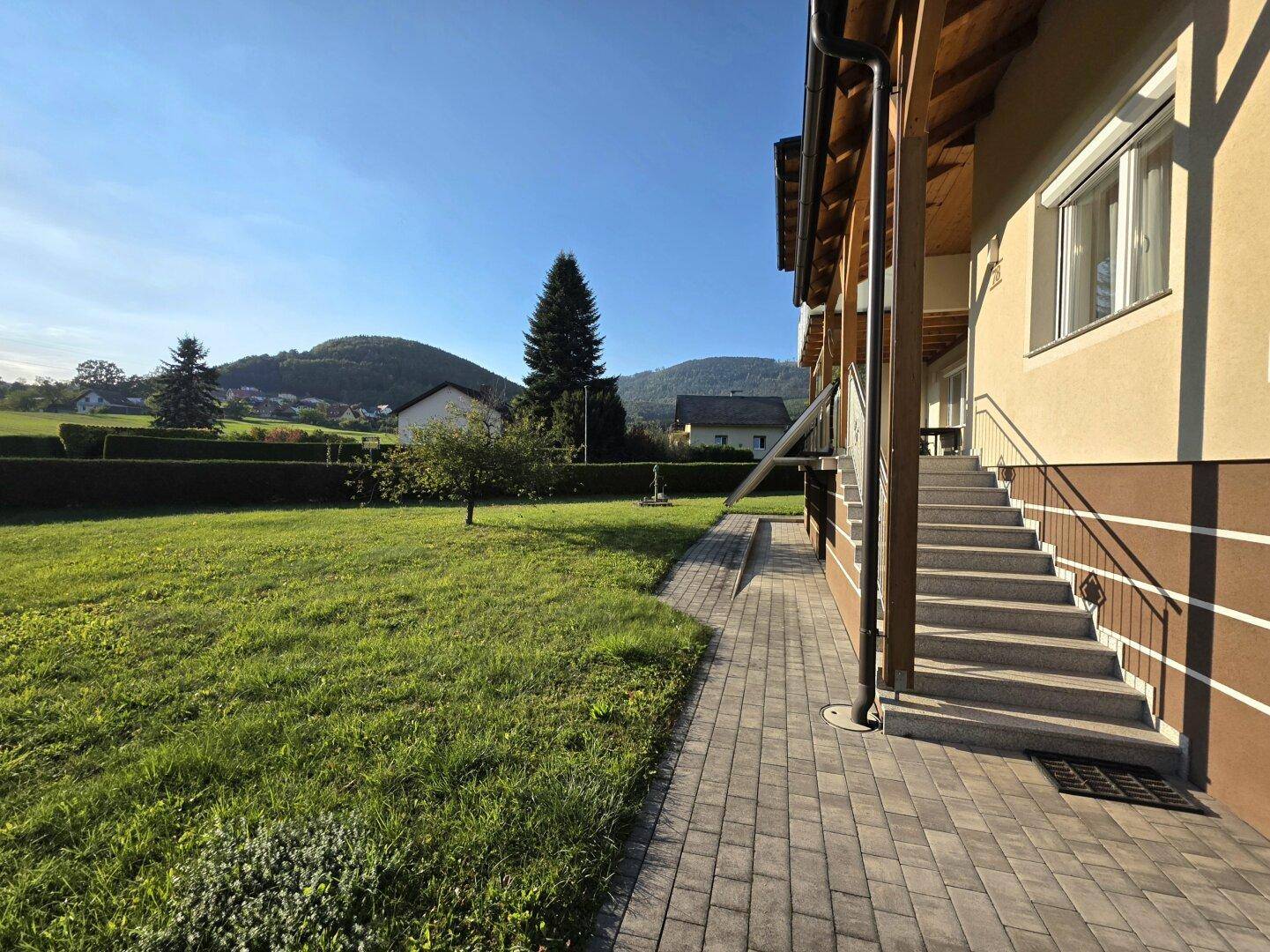 Seitenansicht des Hauses mit gepflastertem Weg, Treppe und weitläufigem Garten.