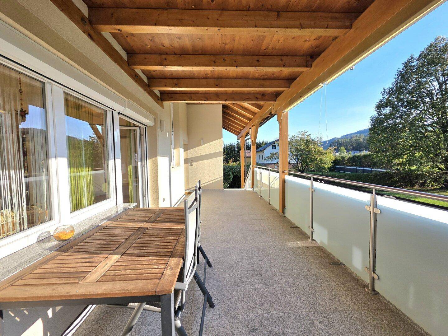 Geräumige, überdachte Terrasse mit Holzbalken und Esstisch, ideal für Mahlzeiten im Freien.
