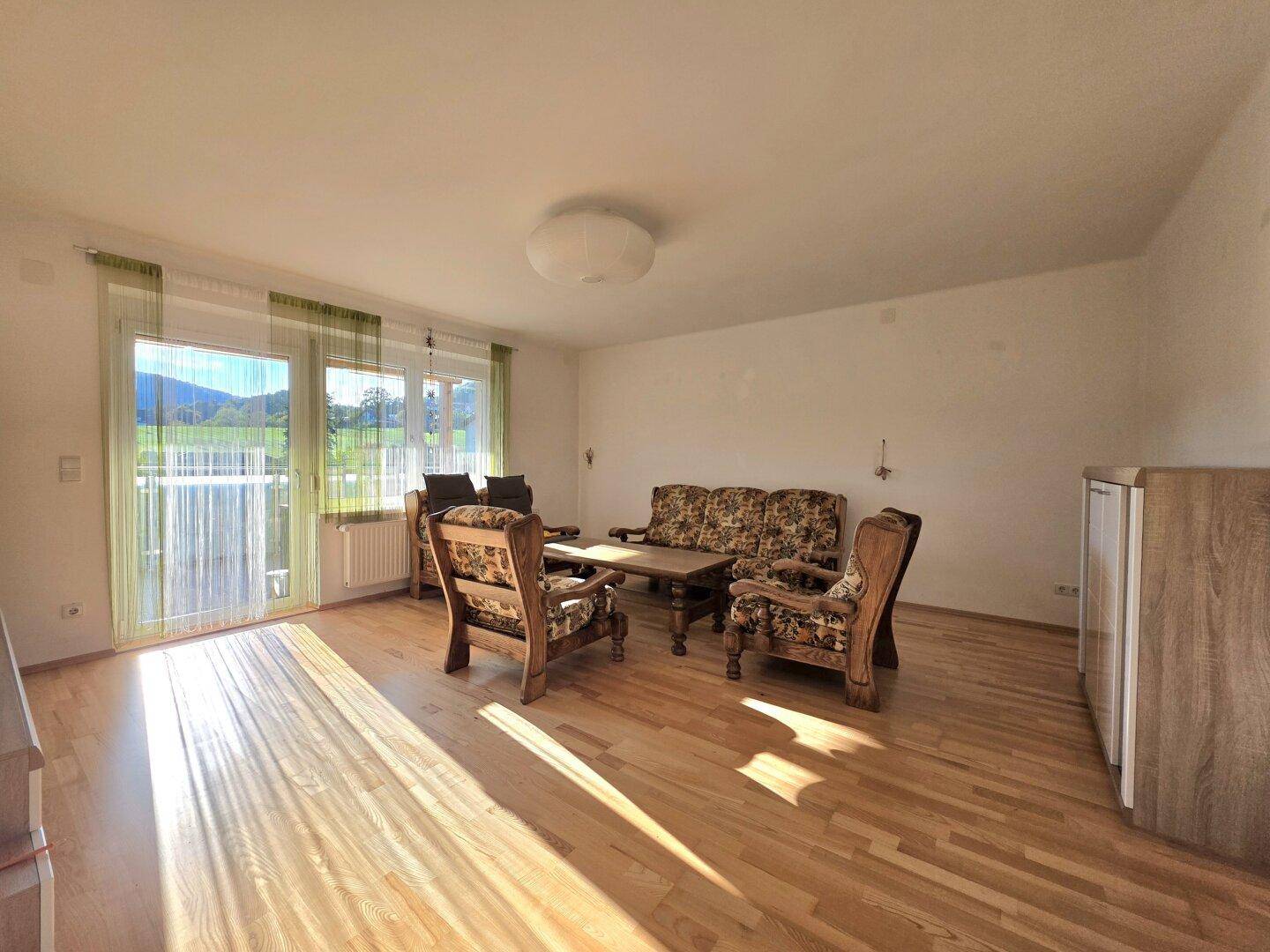 Helles Wohnzimmer mit Holzboden, traditionellen Möbeln und Zugang zum Balkon mit Landschaftsblick.