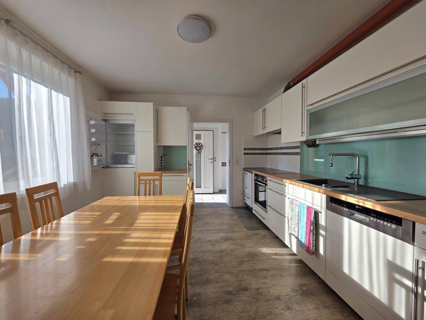 Geräumige Küche mit hellem Holztisch, weißen Schränken und modernen Geräten.