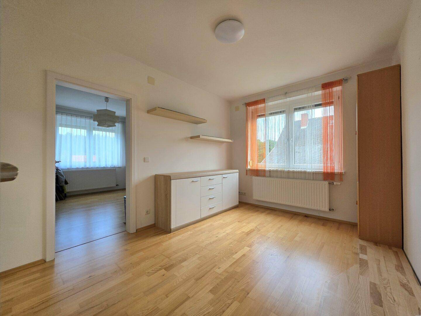 Freundliches Zimmer mit Holzboden, Einbauschränken und Blick auf die Umgebung.