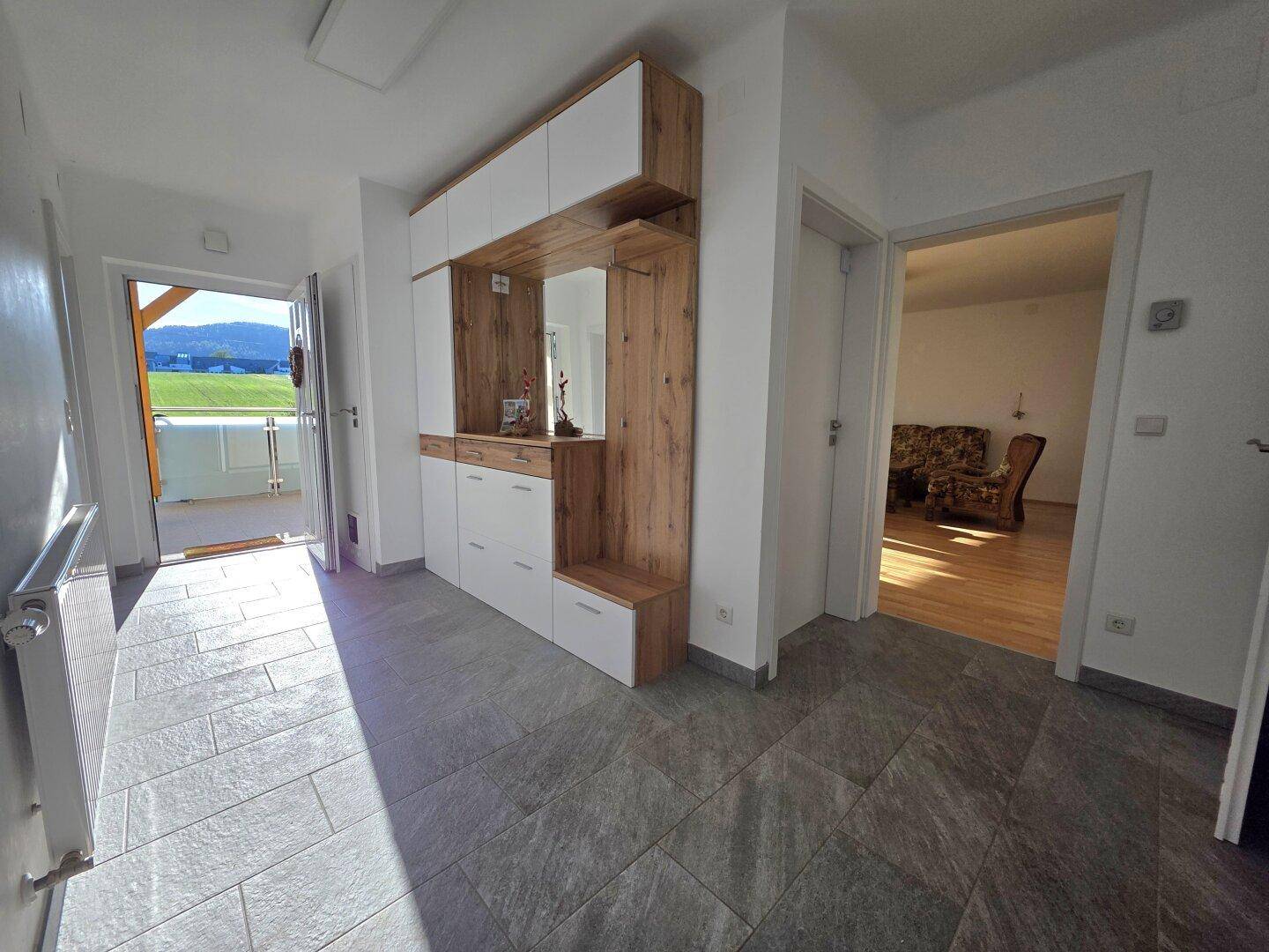 Heller Eingangsbereich mit moderner Garderobe, Fliesenboden und Zugang zum Balkon.