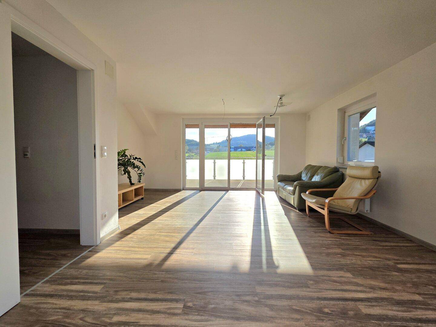 Geräumiges Wohnzimmer mit Laminatboden, großen Fenstern und weitem Blick auf die Landschaft.