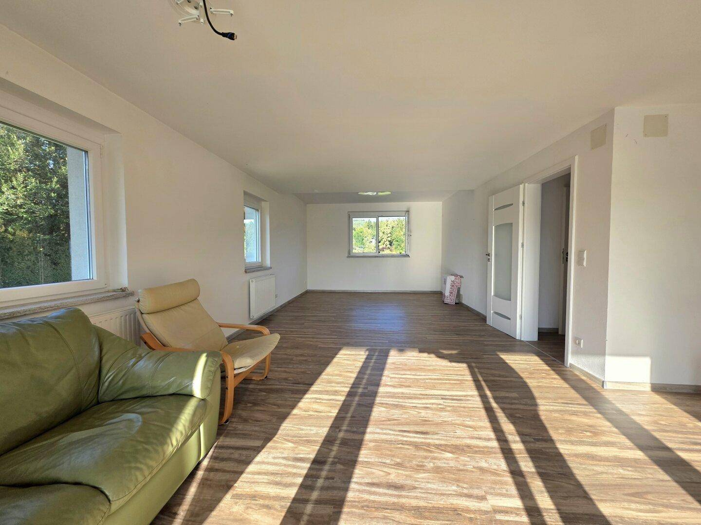 Helles Wohnzimmer mit Laminatboden und mehreren Fenstern, die viel Tageslicht hereinlassen.