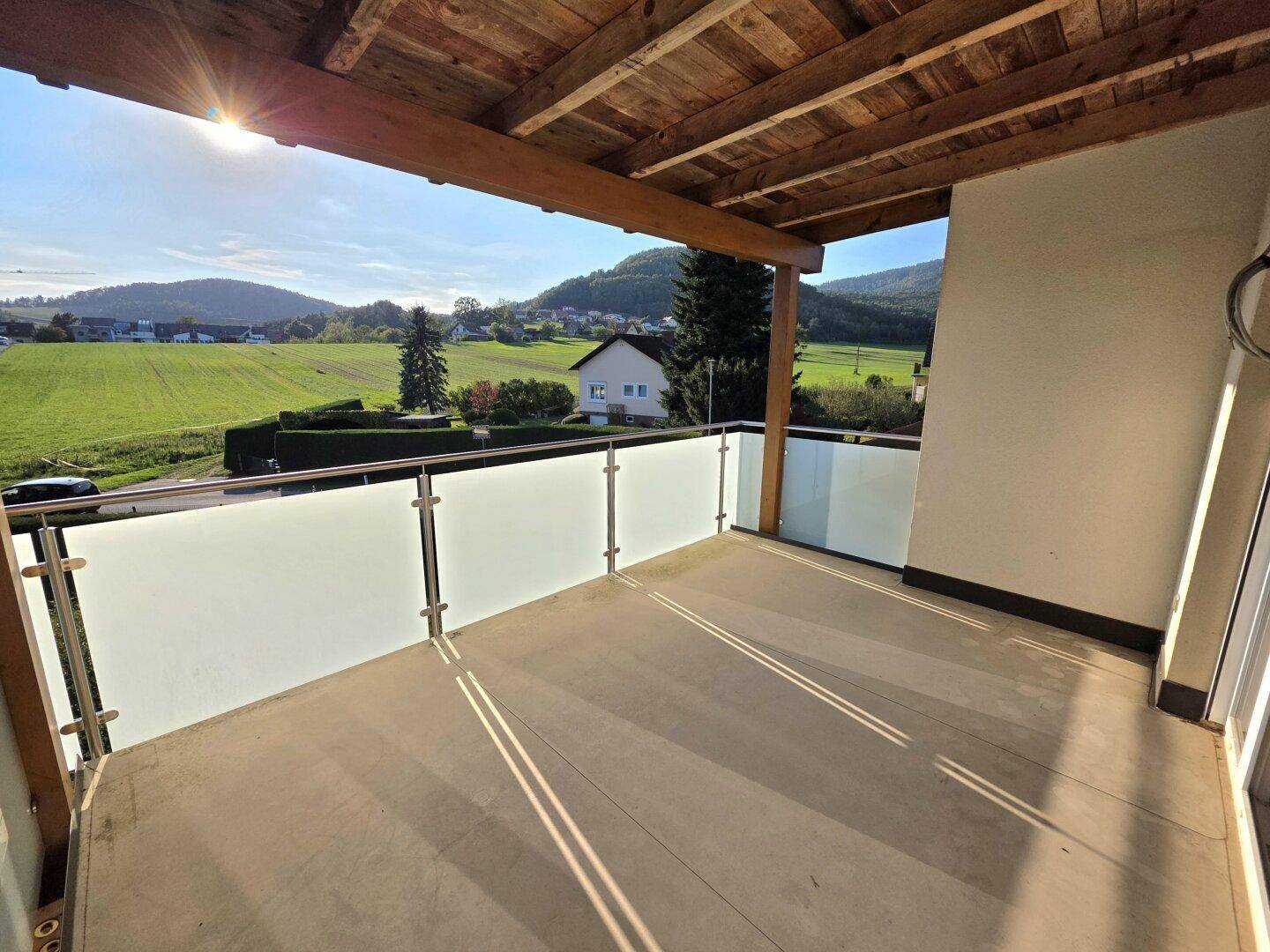 Überdachter Balkon mit Glasgeländer und Panoramablick auf die grüne Hügellandschaft.
