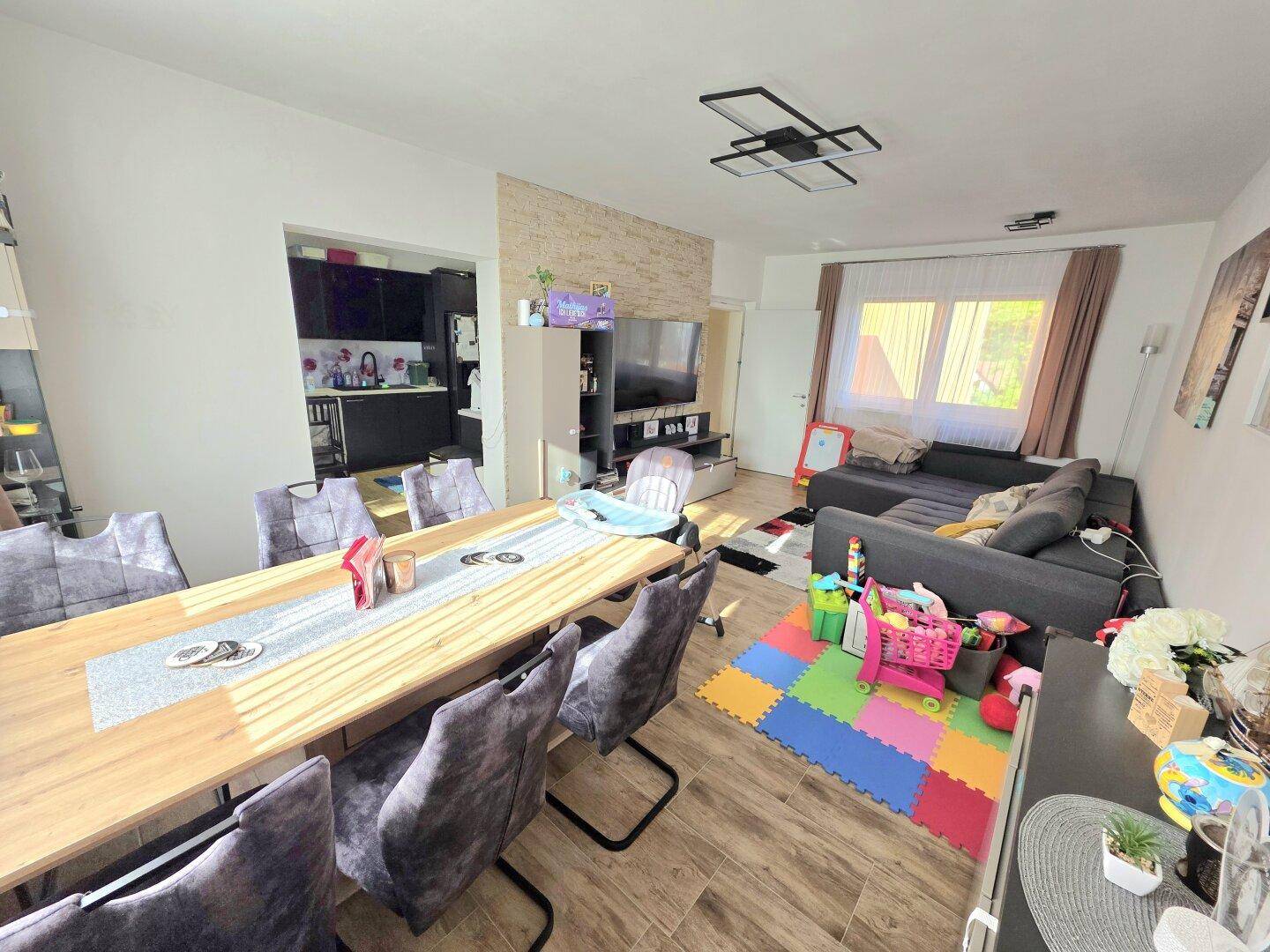 Geräumiger Wohn-Essbereich mit Holztisch, bequemer Couch und offener Verbindung zur Küche.