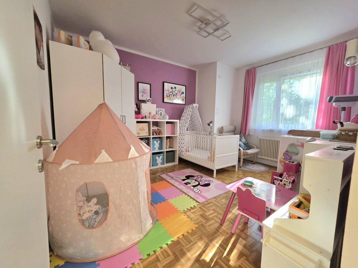 Farbenfrohes Kinderzimmer mit Spielzelt, Babybett und lila Akzentwand.