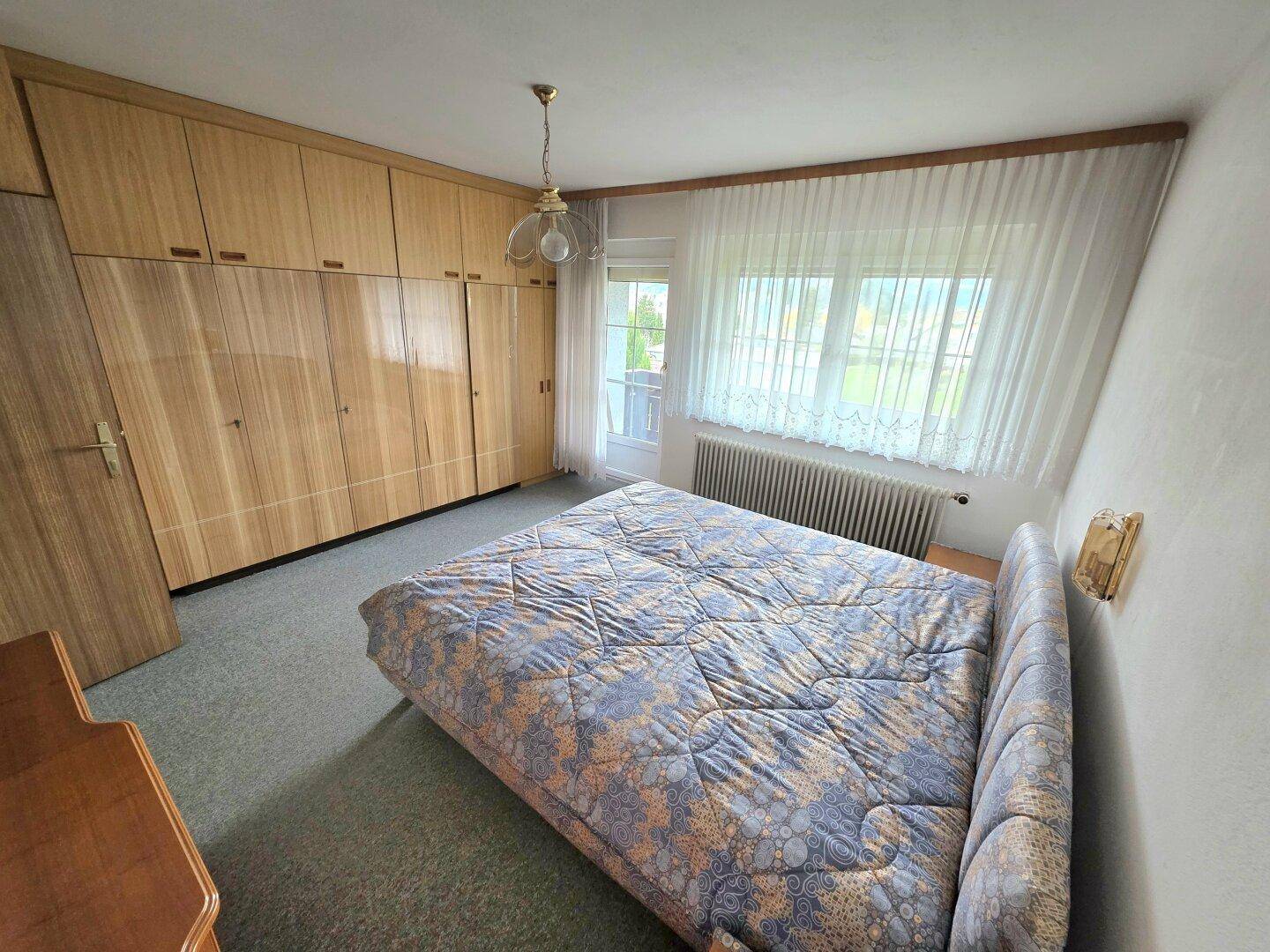 Schlafzimmer mit großem Bett, Holzschrank und Fenster mit Blick ins Grüne.
