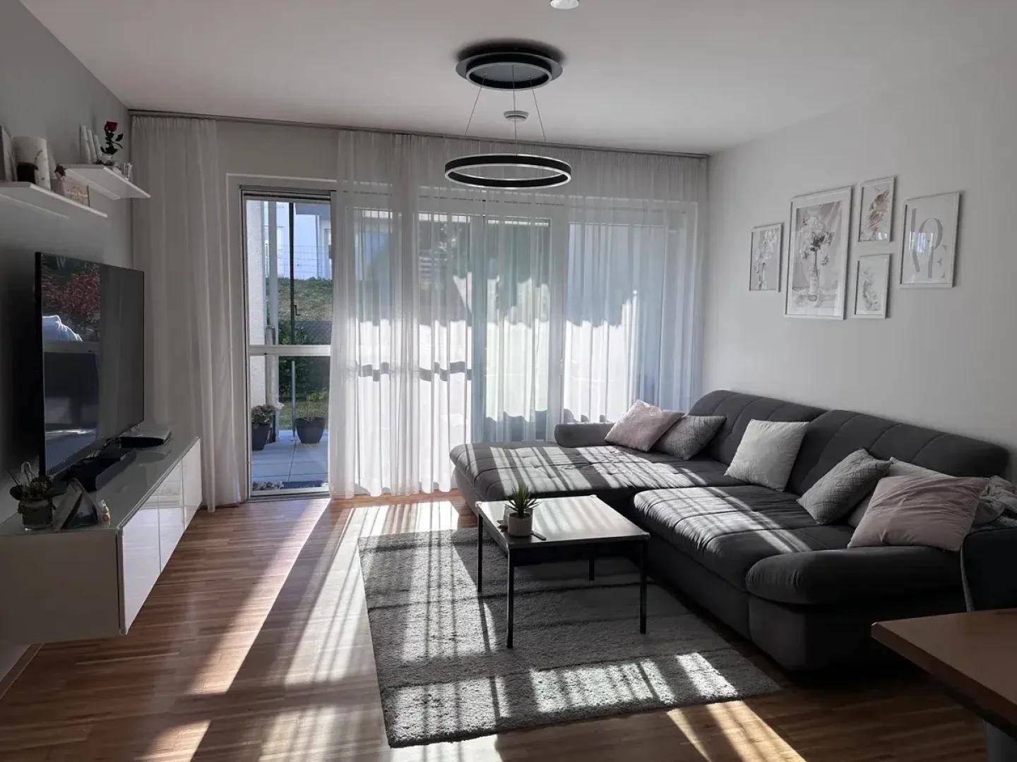 Helles Wohnzimmer mit großem Ecksofa, Holzboden und Zugang zur Terrasse.