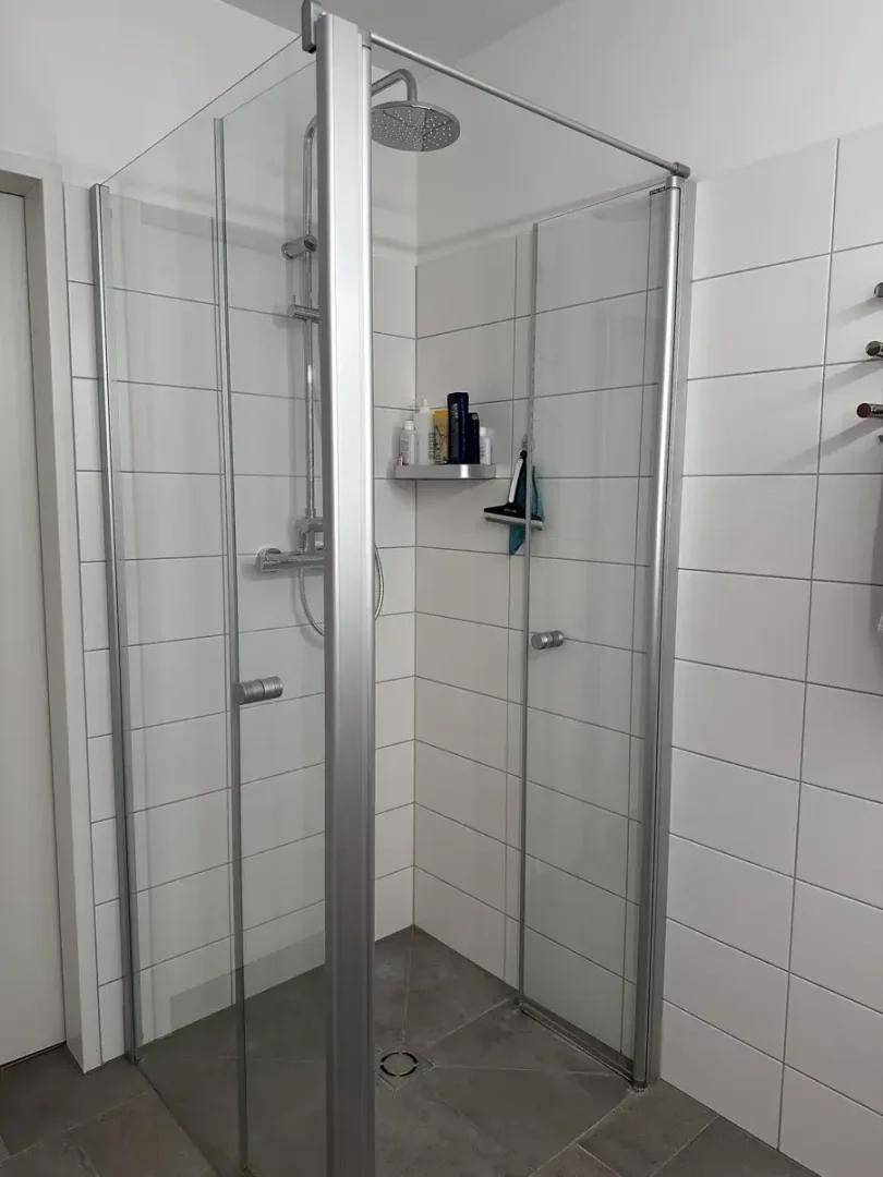 Moderne Duschkabine mit Glaswänden und Regendusche in einem hell gefliesten Badezimmer.