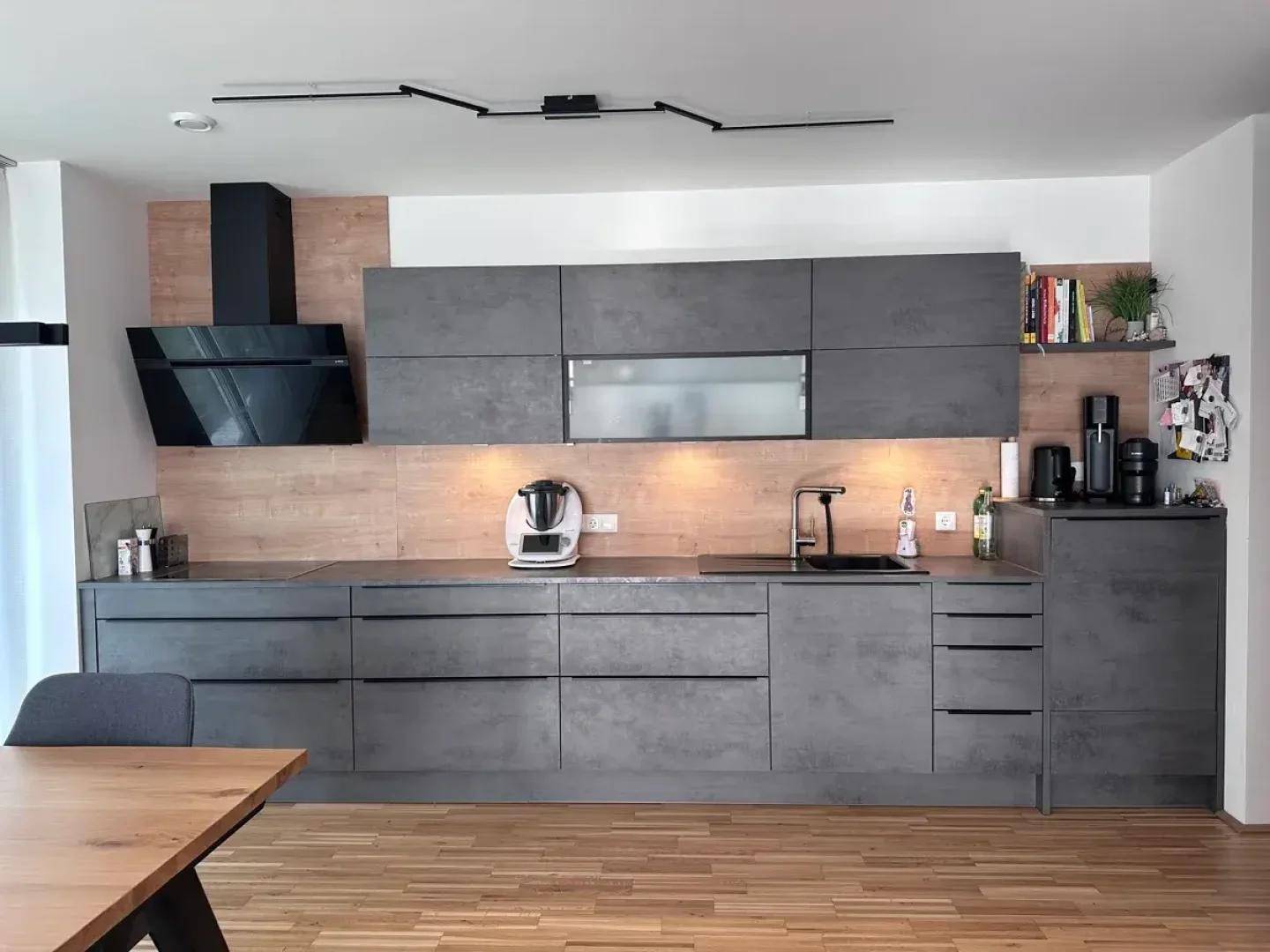 Moderne offene Küche mit grauen Fronten, Holzakzenten und hochwertigen Einbaugeräten.