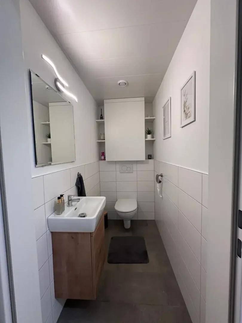 Modernes Gäste-WC mit wandhängendem WC, Holzwaschtisch und weißer Fliesenverkleidung.