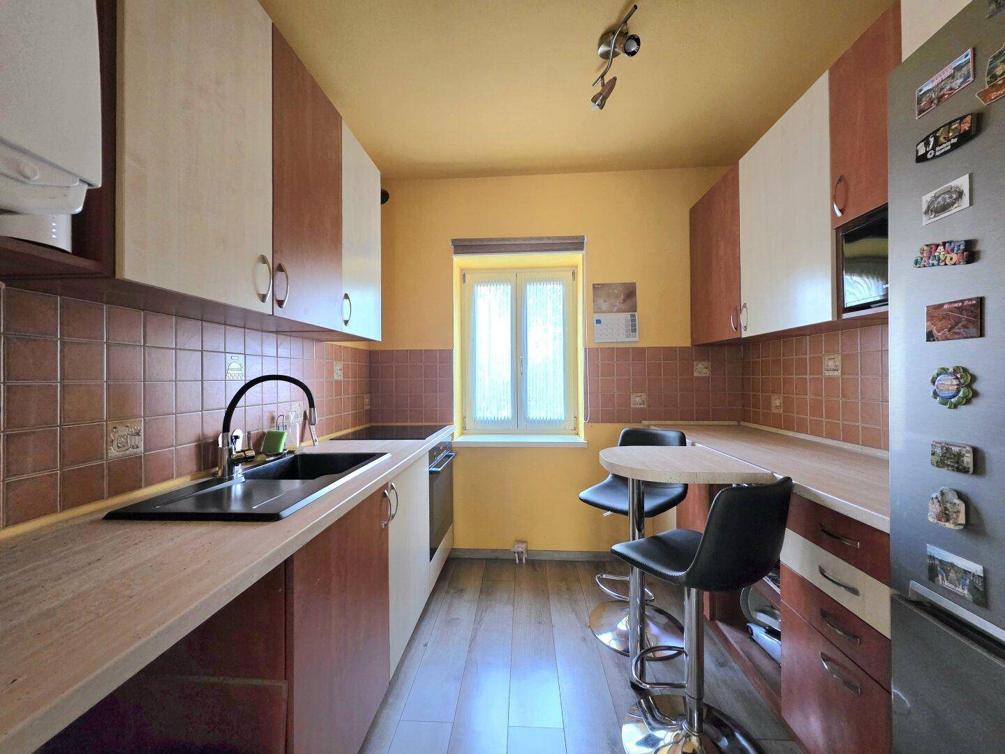 Funktionale Küche mit Holz-Arbeitsplatten, braunen Fliesen und einem kleinen Essbereich.