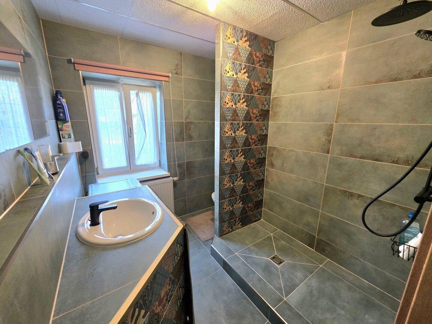 Modernes Badezimmer mit begehbarer Dusche, grünen Fliesen und einem Fenster.