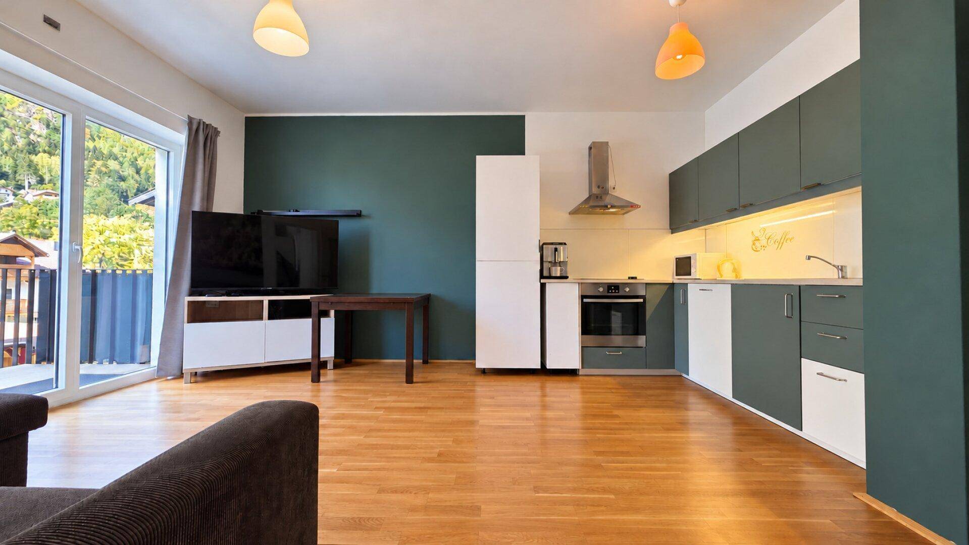 Offener Wohn- und Küchenbereich mit Holzboden, Sofa und Zugang zum Außenbereich.