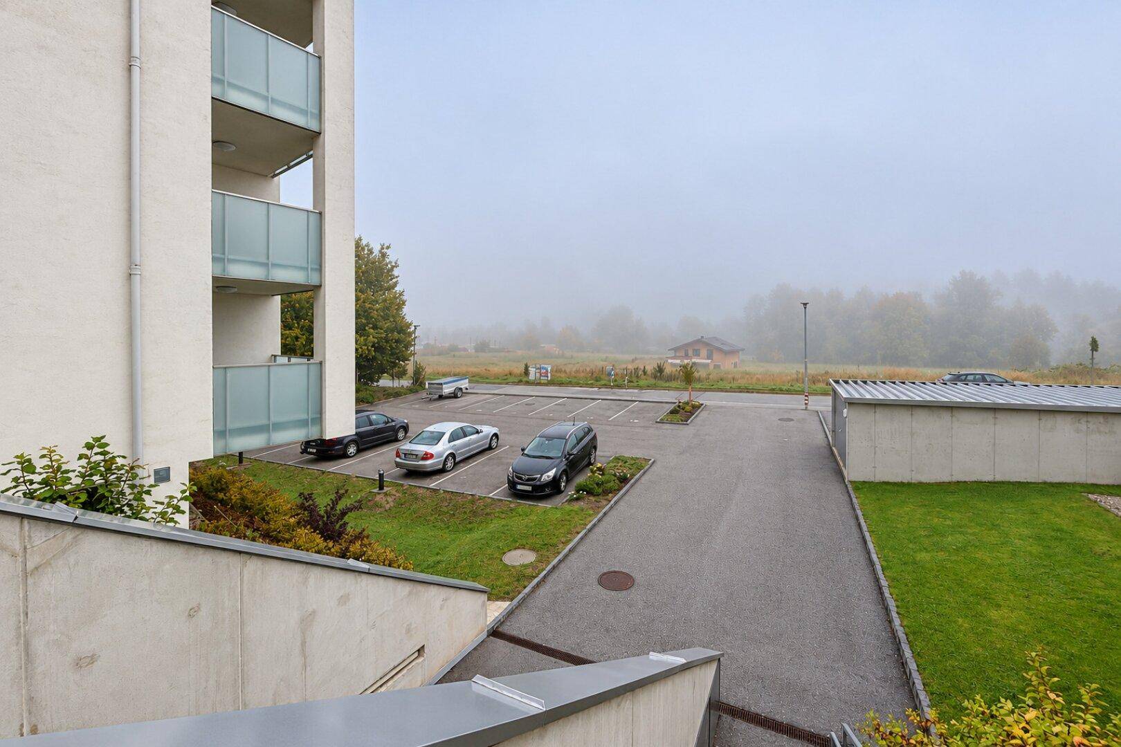 Außenansicht des Apartmentgebäudes mit Parkplätzen und ländlicher Umgebung im Nebel.