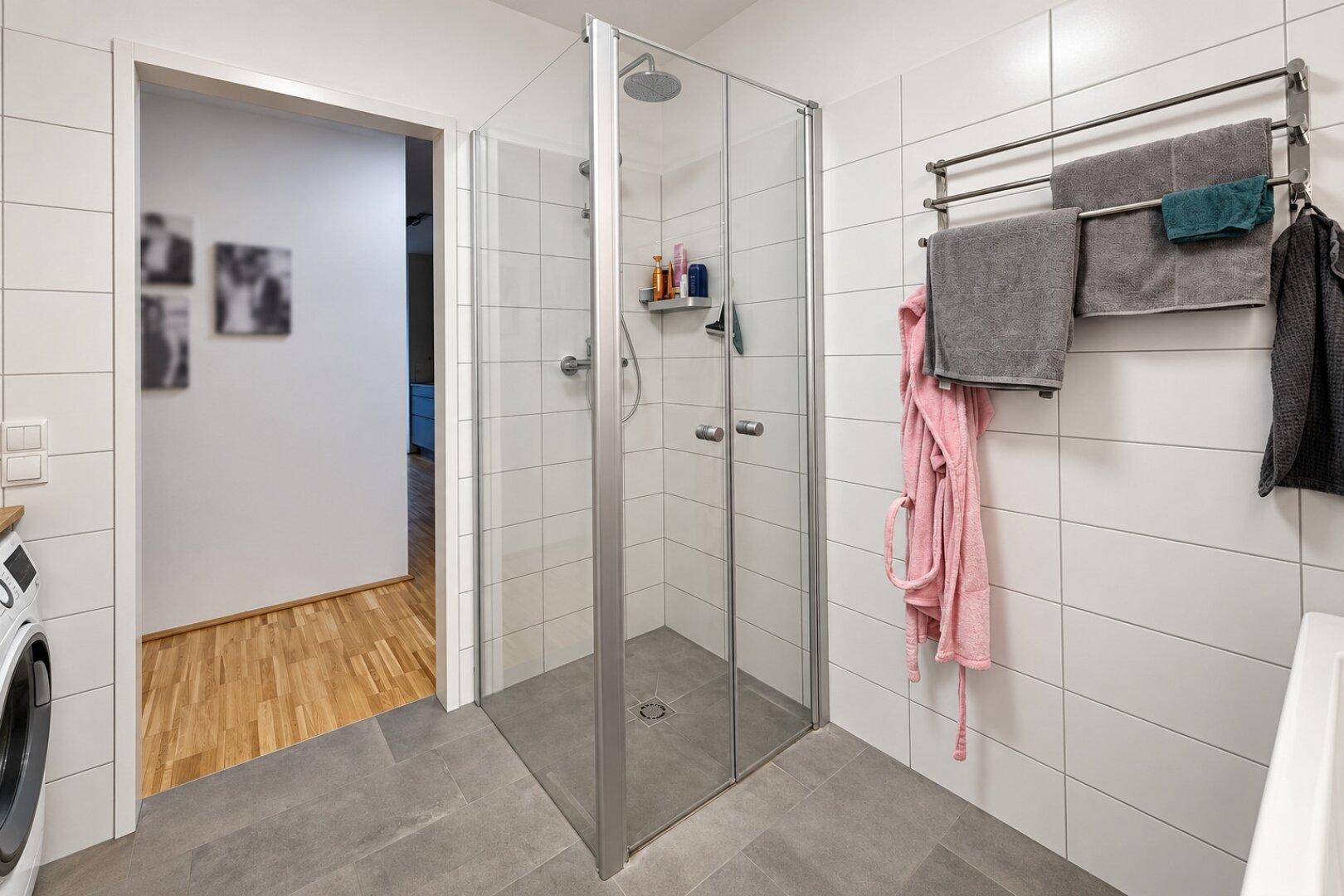 Modernes Badezimmer mit begehbarer Dusche, weißen Wandfliesen und praktischem Handtuchhalter.