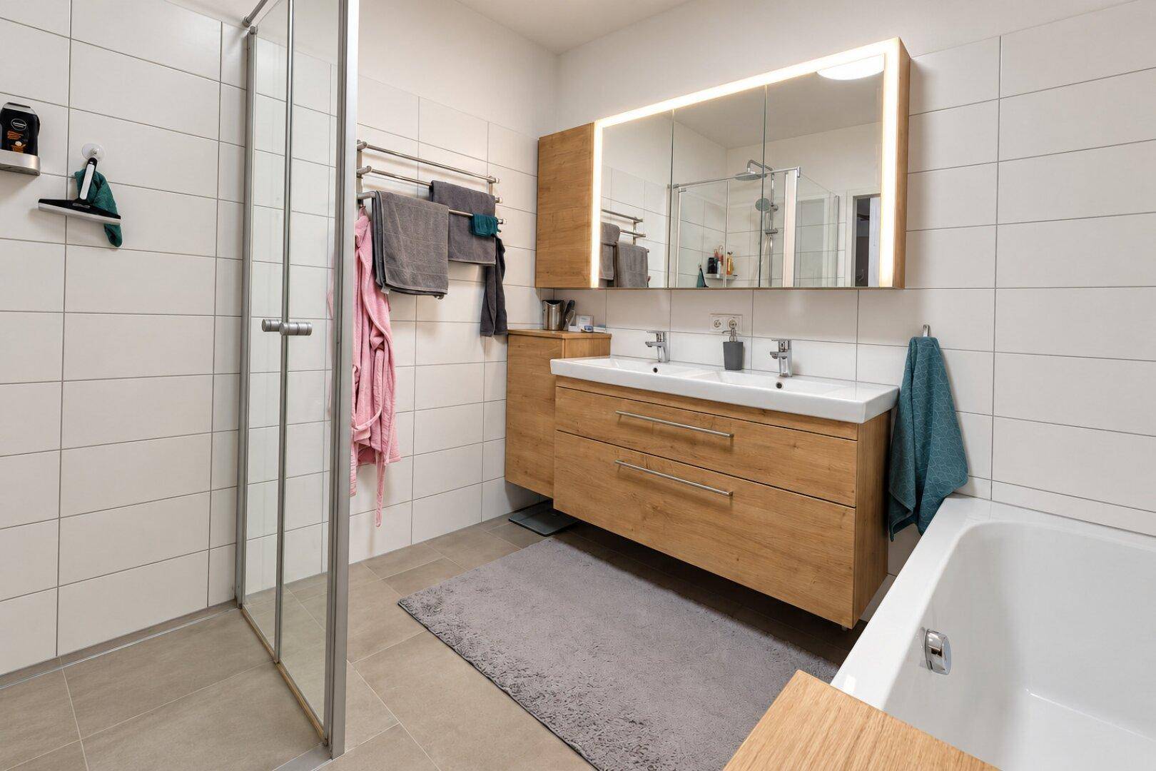 Geräumiges Badezimmer mit Doppelwaschbecken, beleuchtetem Spiegelschrank, Dusche und Badewanne.