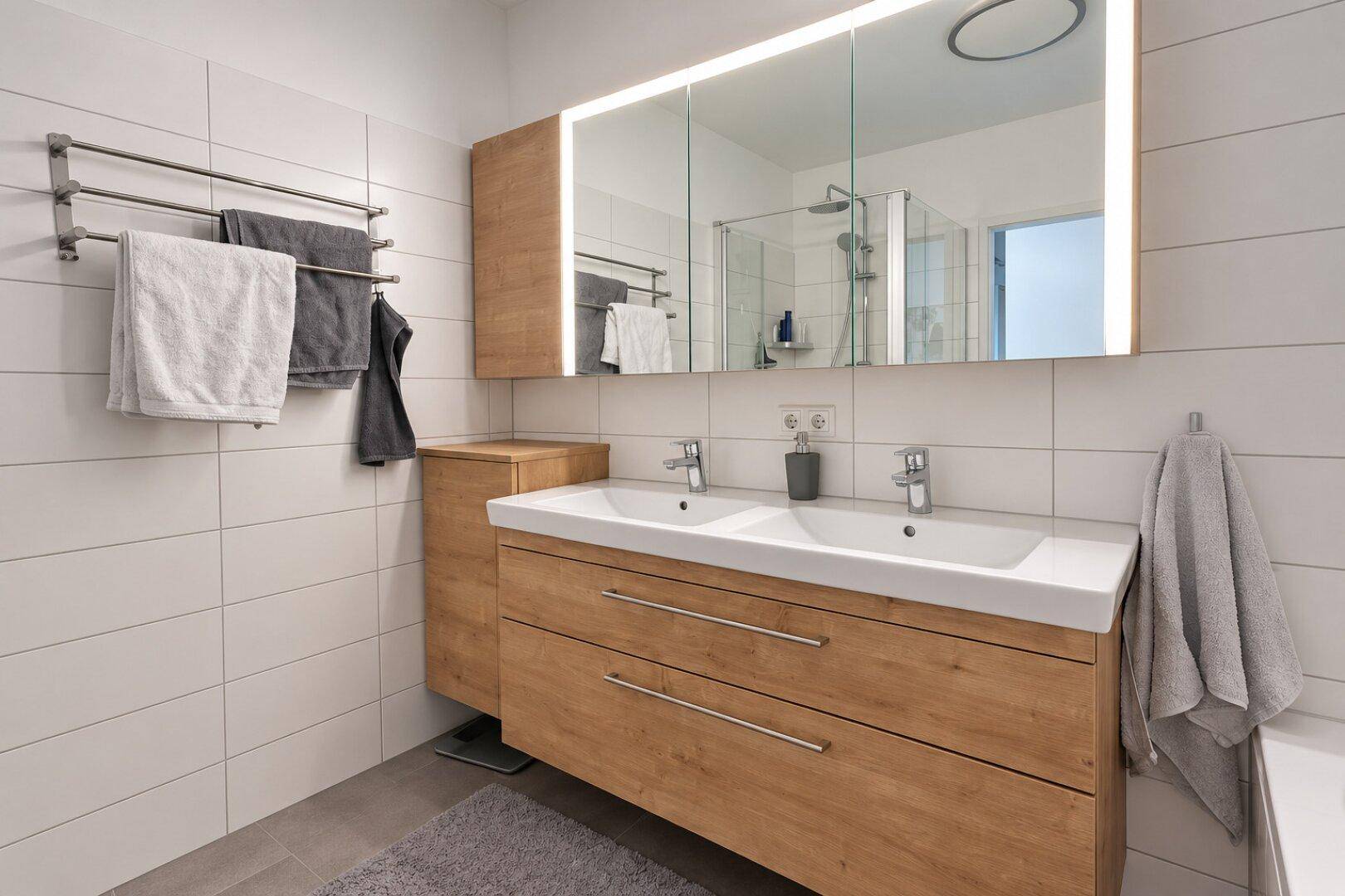 Helles Badezimmer mit modernem Doppelwaschbecken, großem Spiegelschrank und Holzunterschrank.