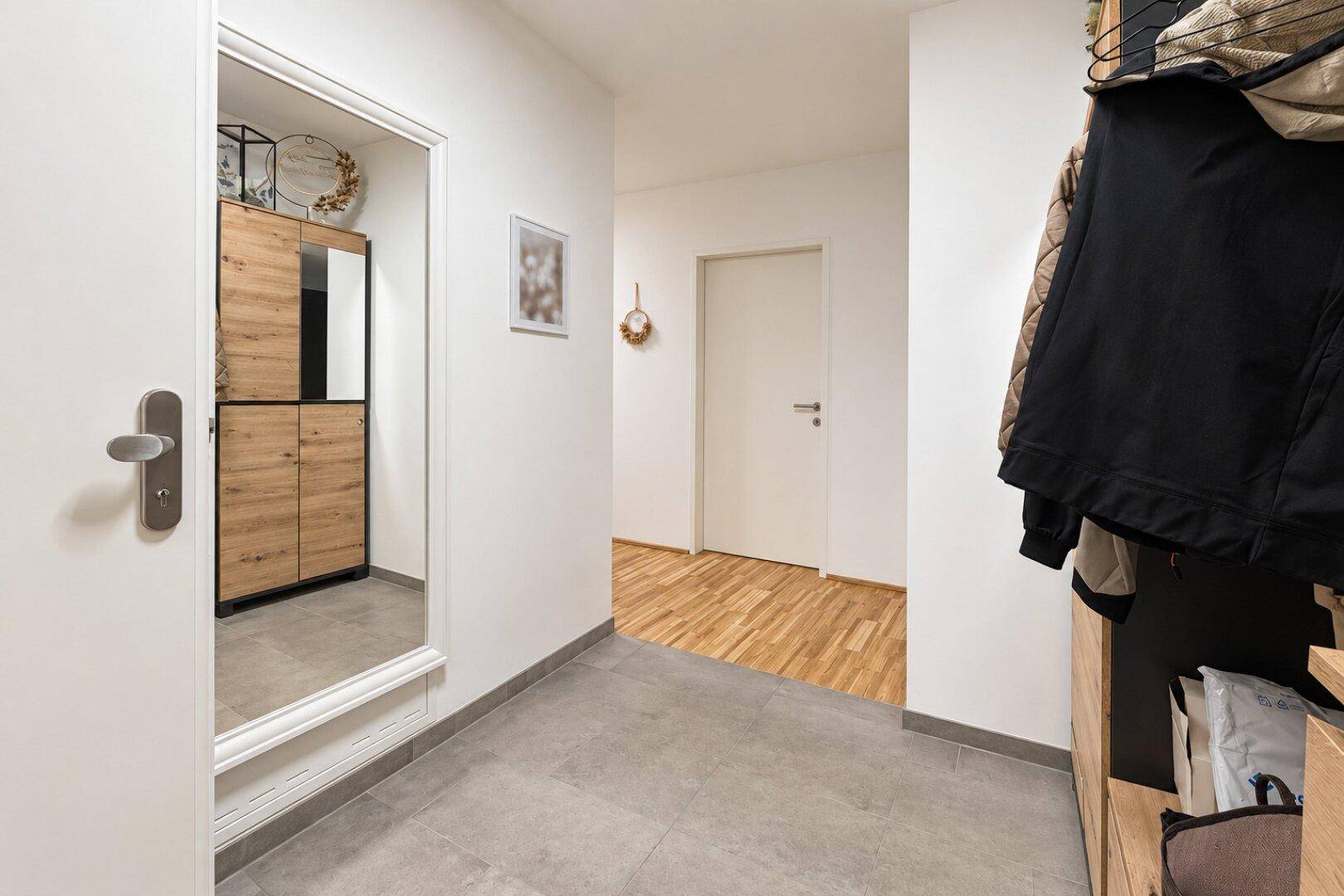 Heller Eingangsbereich mit großem Spiegel, Holzmöbeln und modernem Fliesenboden.