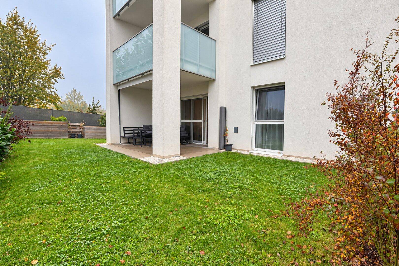 Gepflegter Gartenbereich mit Terrasse und Sitzgelegenheiten im Erdgeschoss des modernen Gebäudes.