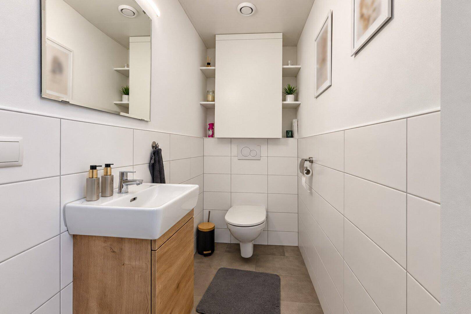 Modernes Gäste-WC mit Waschbecken, wandhängender Toilette und weißen Fliesen.