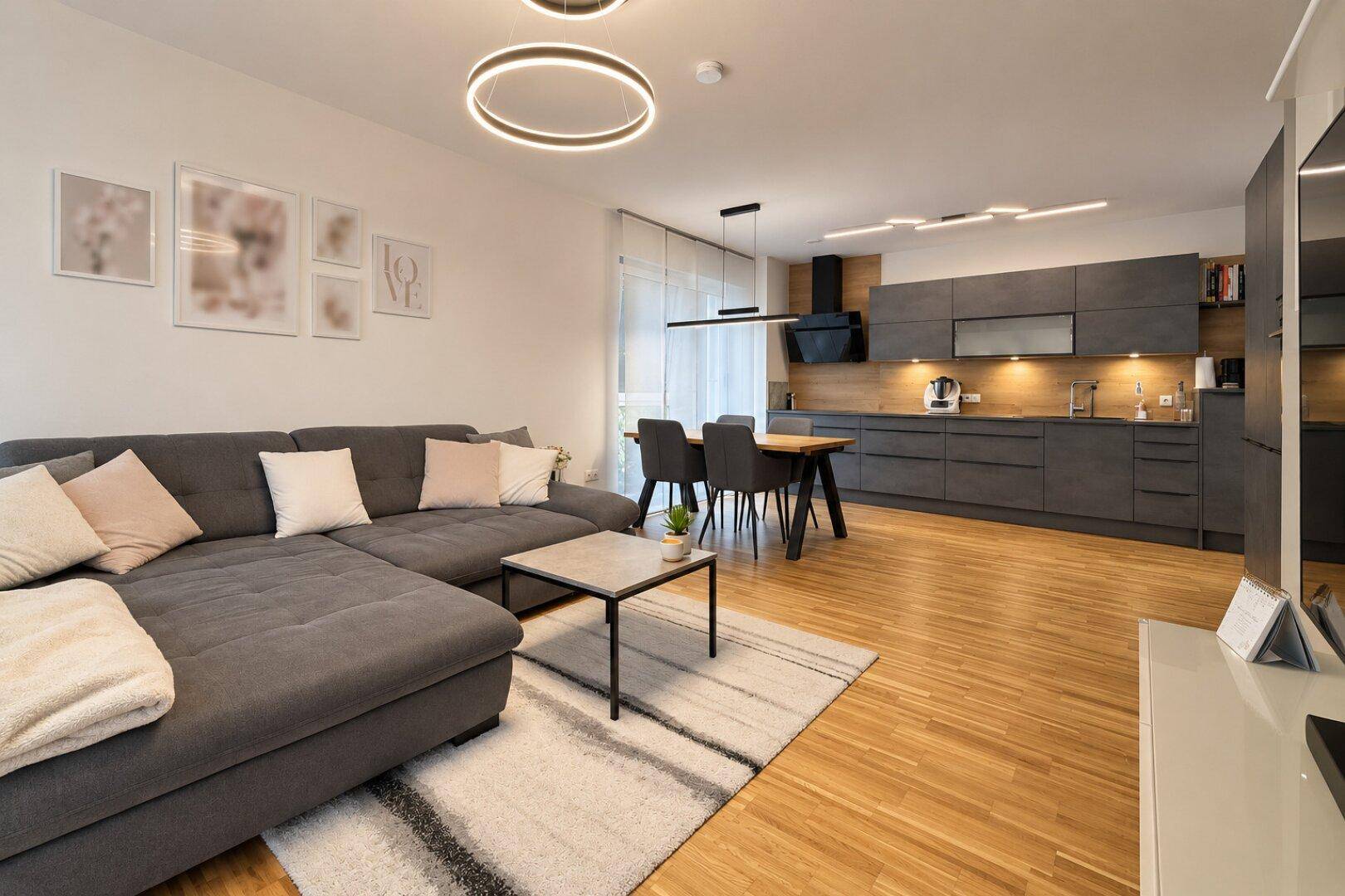 Offener Wohnbereich mit gemütlichem Sofa und integrierter, moderner Küche mit dunklen Schränken.
