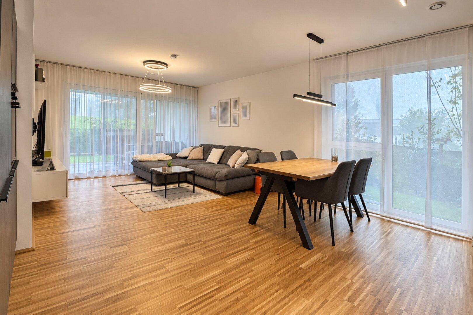 Heller Wohn- und Essbereich mit modernem Design, Holzboden und großen Fenstern zum Garten.