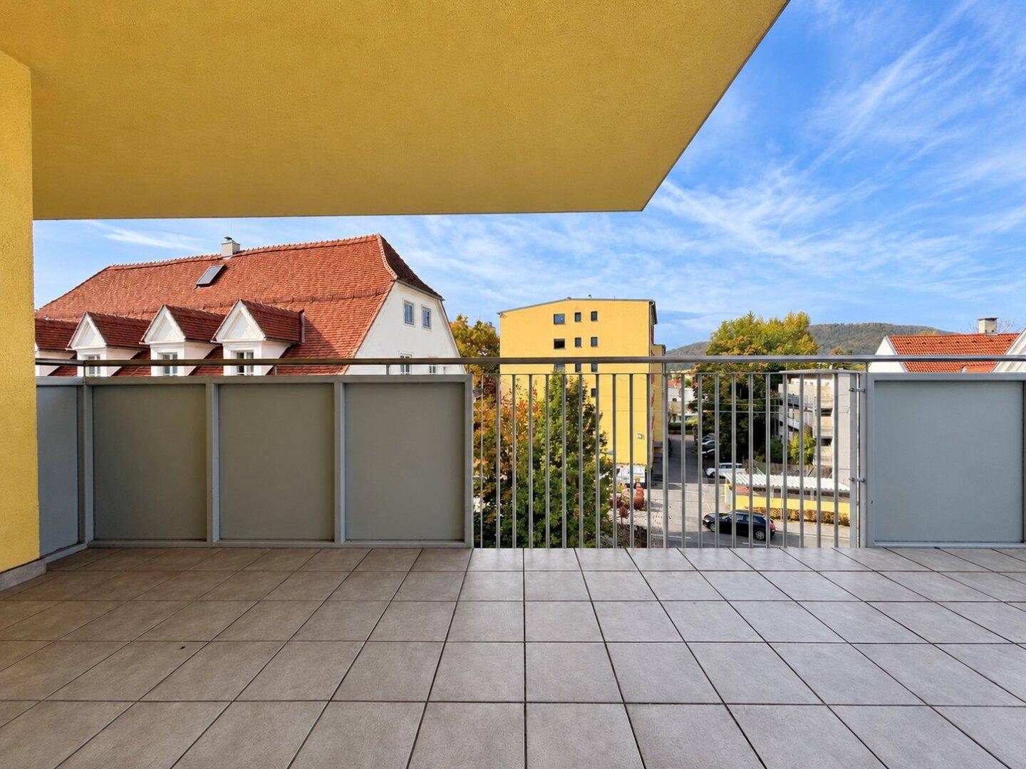 Geräumiger Balkon mit Fliesenboden und Blick auf die umliegenden Gebäude und Landschaft.