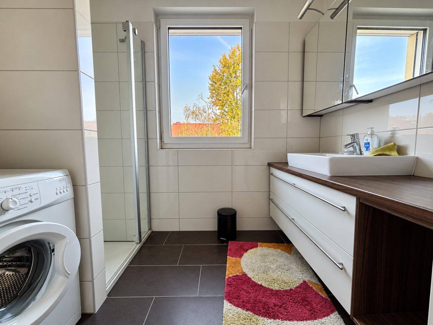 Modernes Badezimmer mit Dusche, Waschbecken, Spiegelschrank und Waschmaschine.