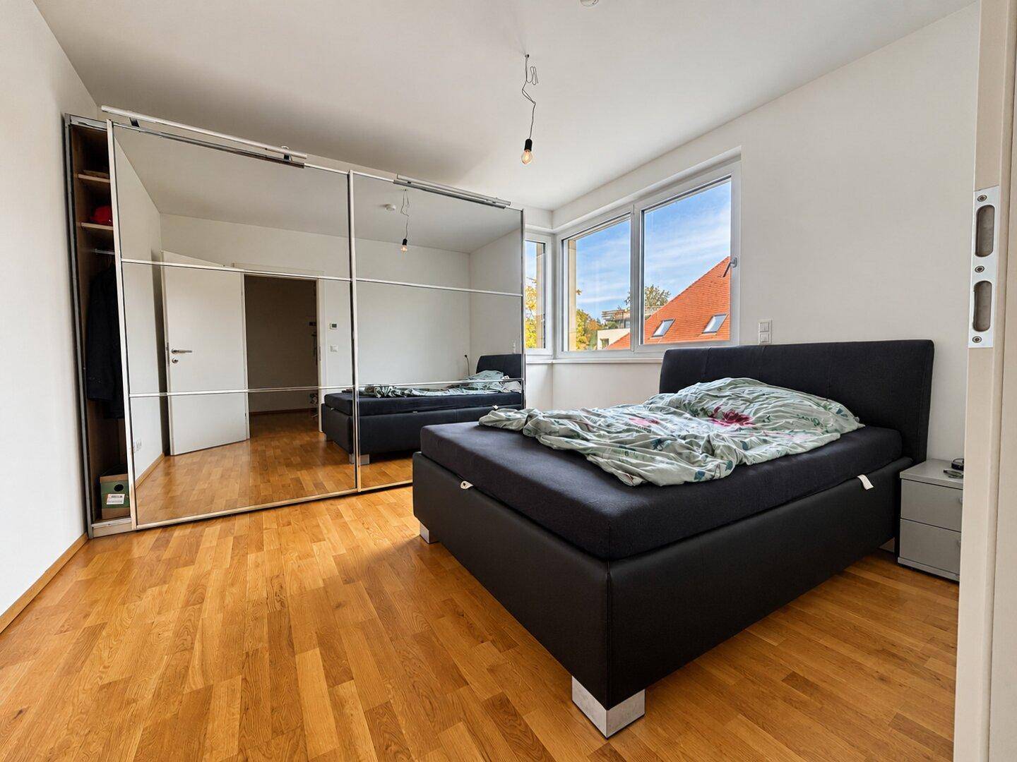 Helles Schlafzimmer mit großem Spiegelschrank, Doppelbett und Parkettboden.