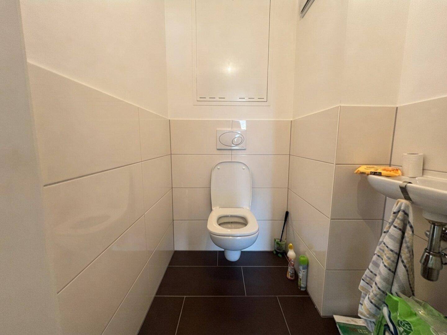 Kleines separates WC mit Wand-WC, Handwaschbecken und Fliesen an Wänden und Boden.