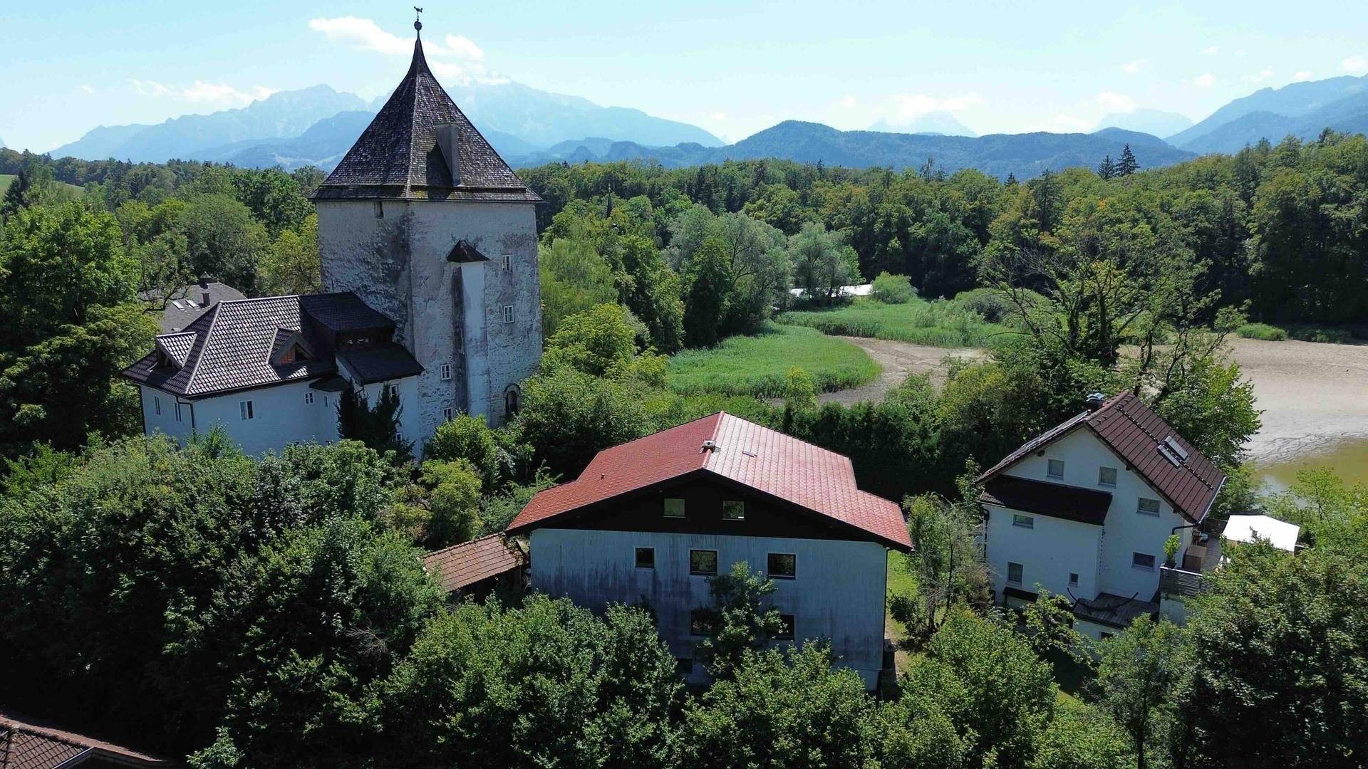 Weitläufige Landschaftsaufnahme mit historischem Turm, mehreren Häusern und Bergen im Hintergrund.