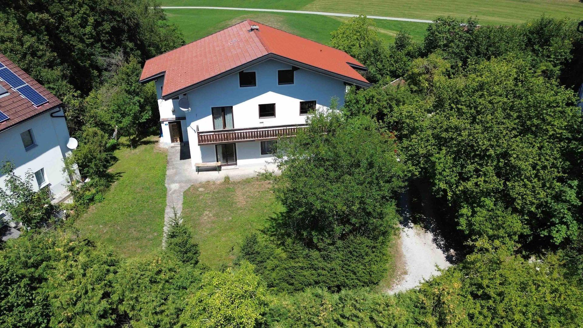 Luftaufnahme eines Einfamilienhauses mit rotem Dach und Balkon, umgeben von üppiger grüner Landschaft.