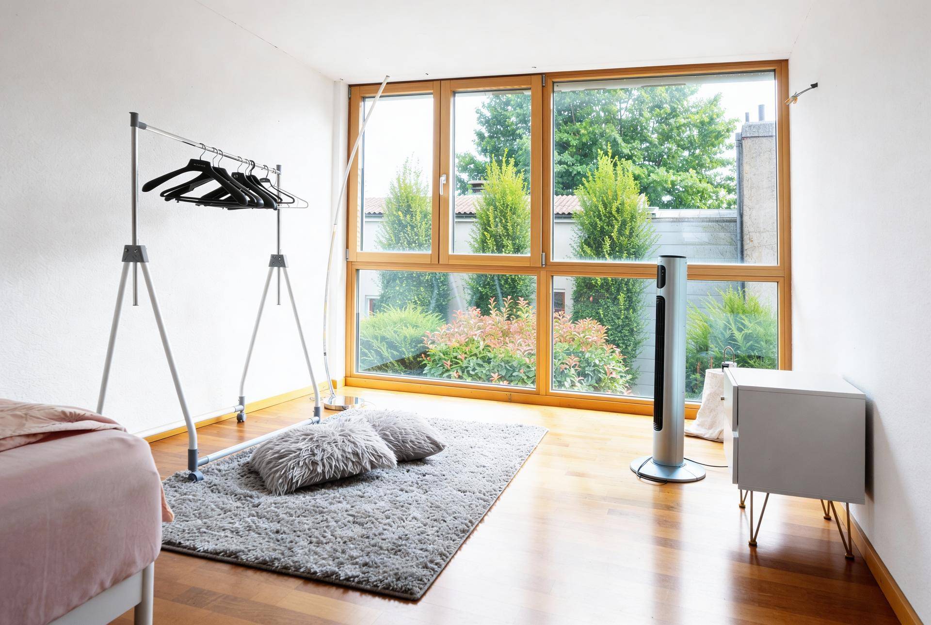 Schlafzimmer mit großen Fenstern, Holzboden und Blick ins Grüne.
