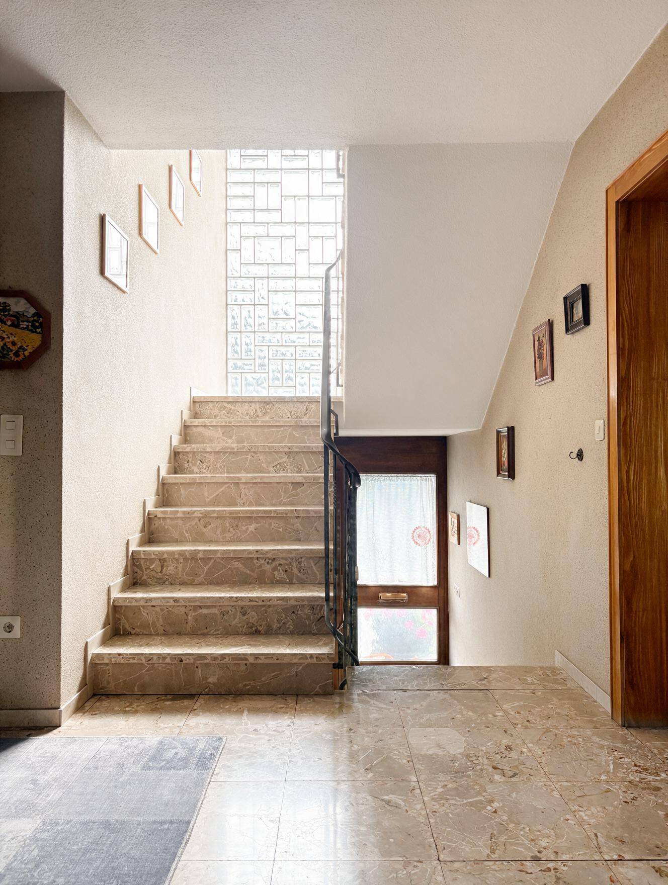 Heller Flur mit Marmorfliesen, Treppe und Glasbausteinwand, die für natürliches Licht sorgt.