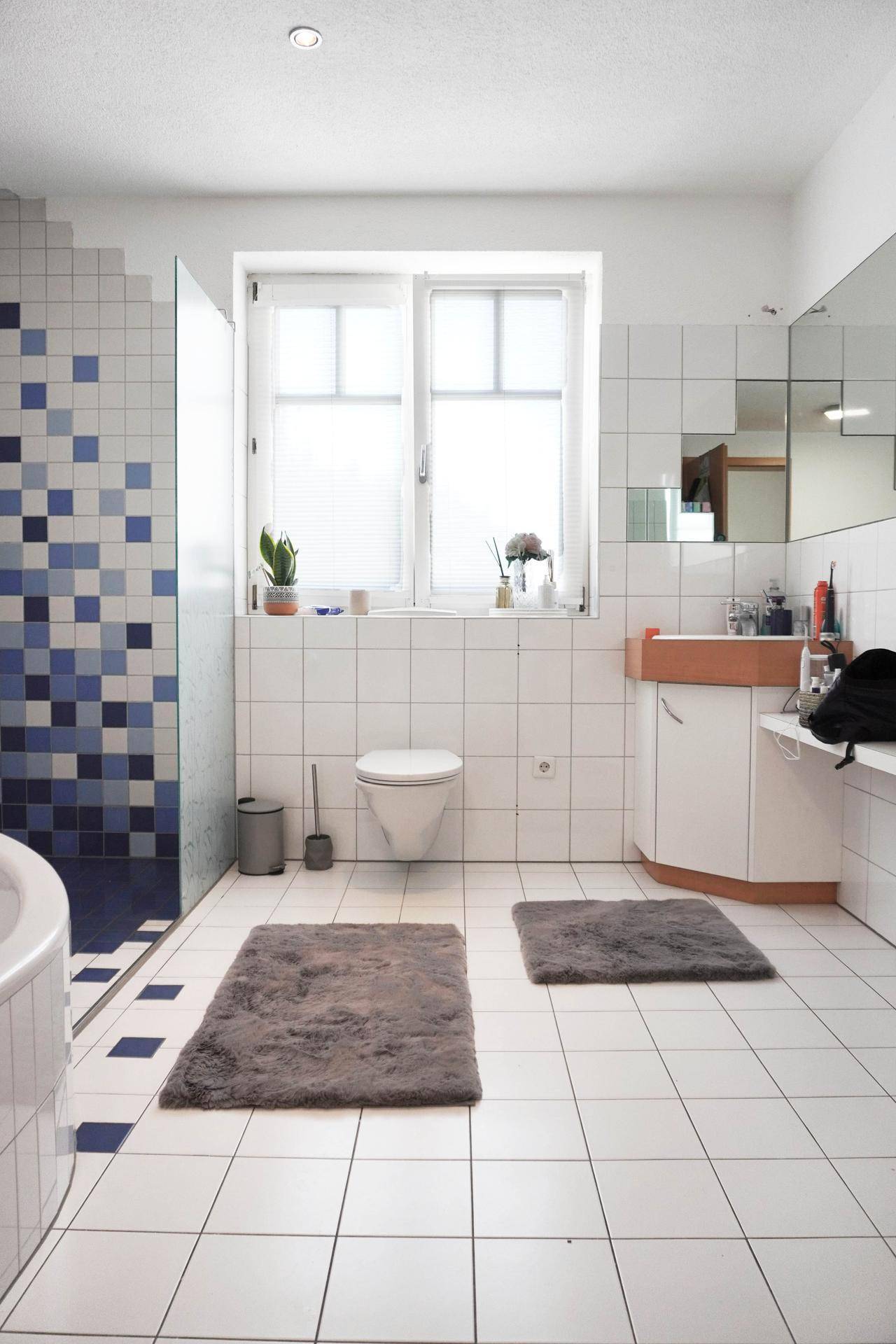 Helles Badezimmer mit Fenster, WC, Waschbecken und weißen Fliesen.
