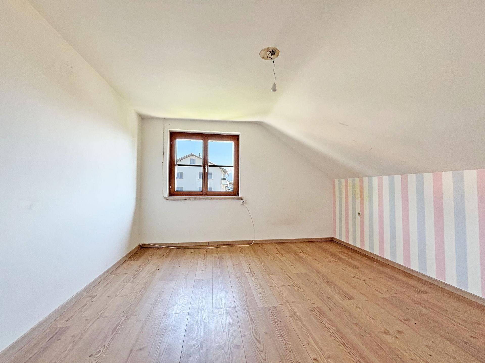 Dachgeschosszimmer mit Laminatboden, schrägen Wänden und einem Fenster, das Tageslicht spendet.