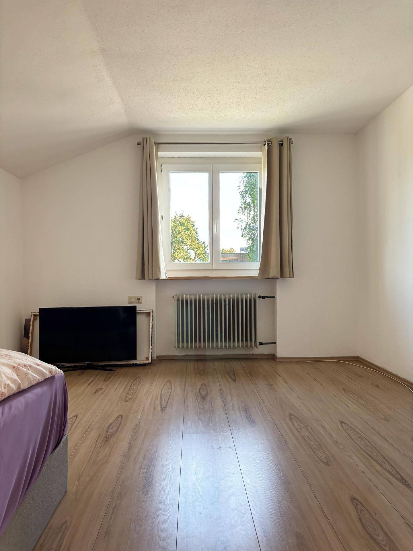 Helles Zimmer mit Laminatboden und einem Fenster, das viel Tageslicht hereinlässt.