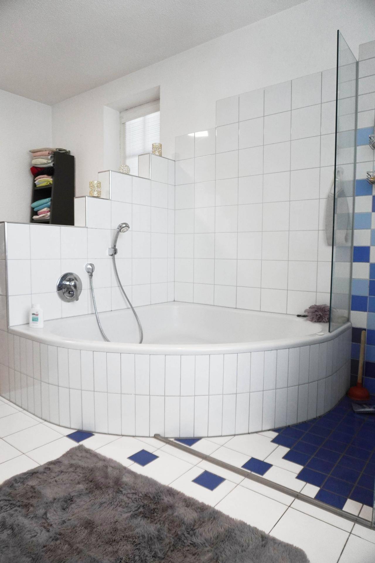 Badezimmer mit Eckbadewanne, weißen Fliesen und blauen Akzenten.