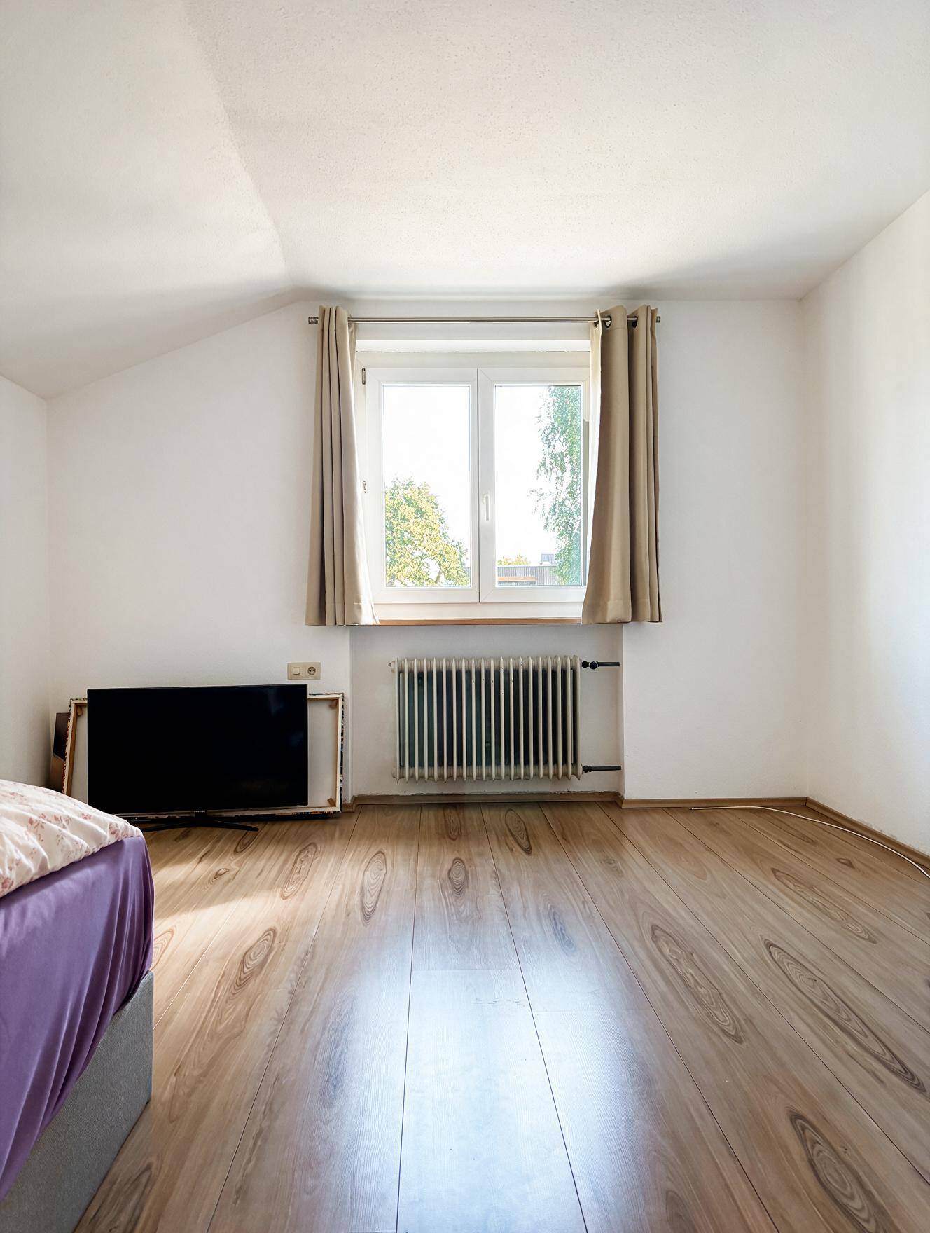 Schlafzimmer mit Laminatboden, Dachschräge und Fenster mit Blick ins Grüne, hell und freundlich.