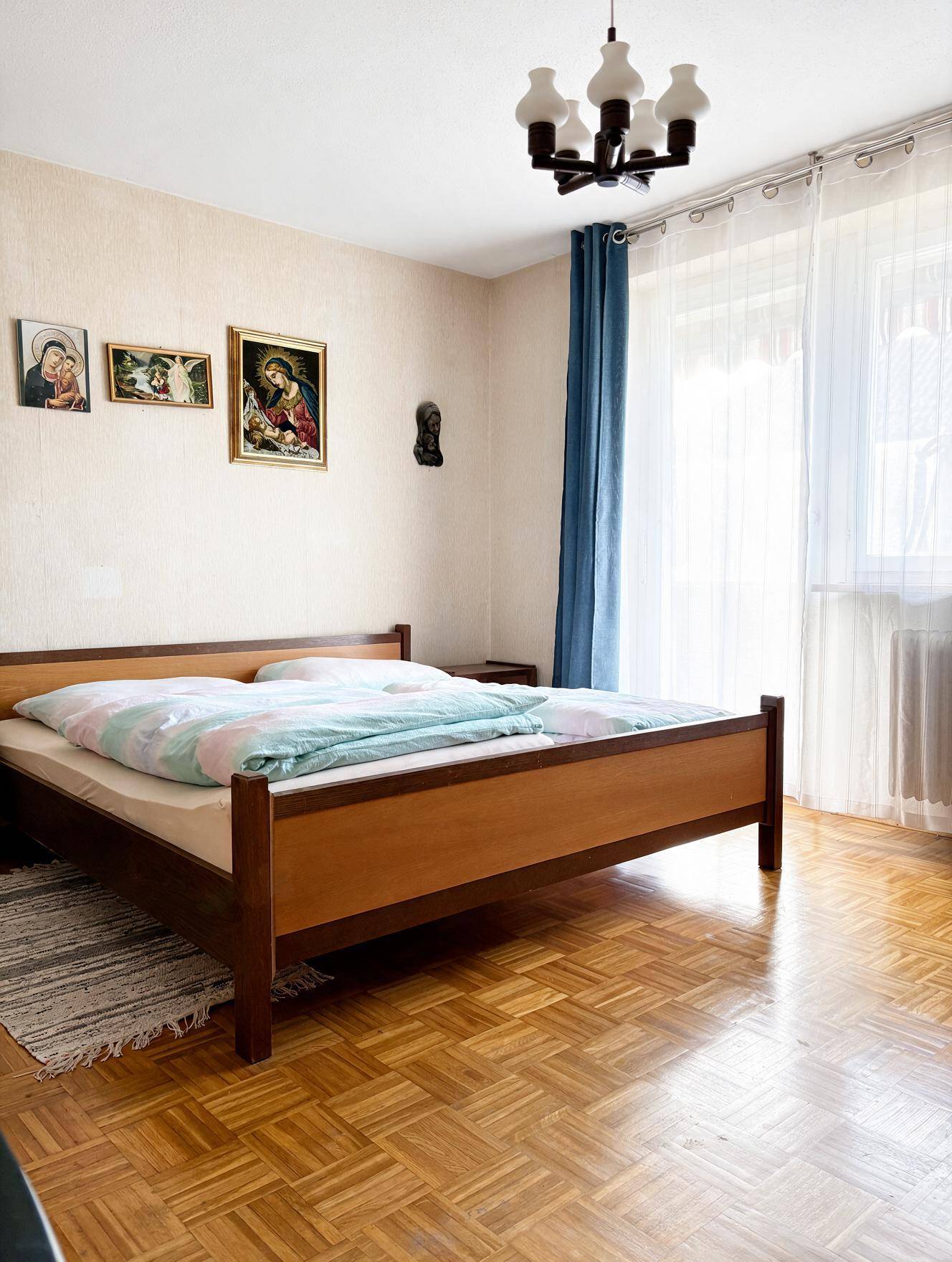 Helles Schlafzimmer mit Parkettboden, Doppelbett und großem Fenster, das viel Tageslicht hereinlässt.