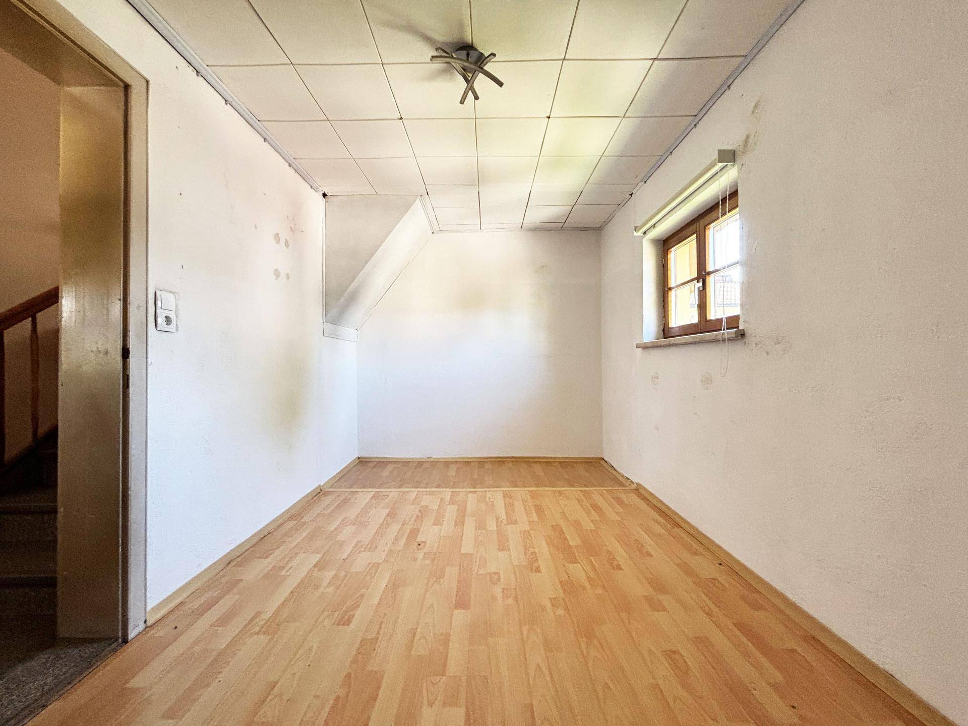 Raum mit Laminatboden, Fenster und Zugang zu einer Treppe, möglicherweise ein Flur oder Abstellraum.