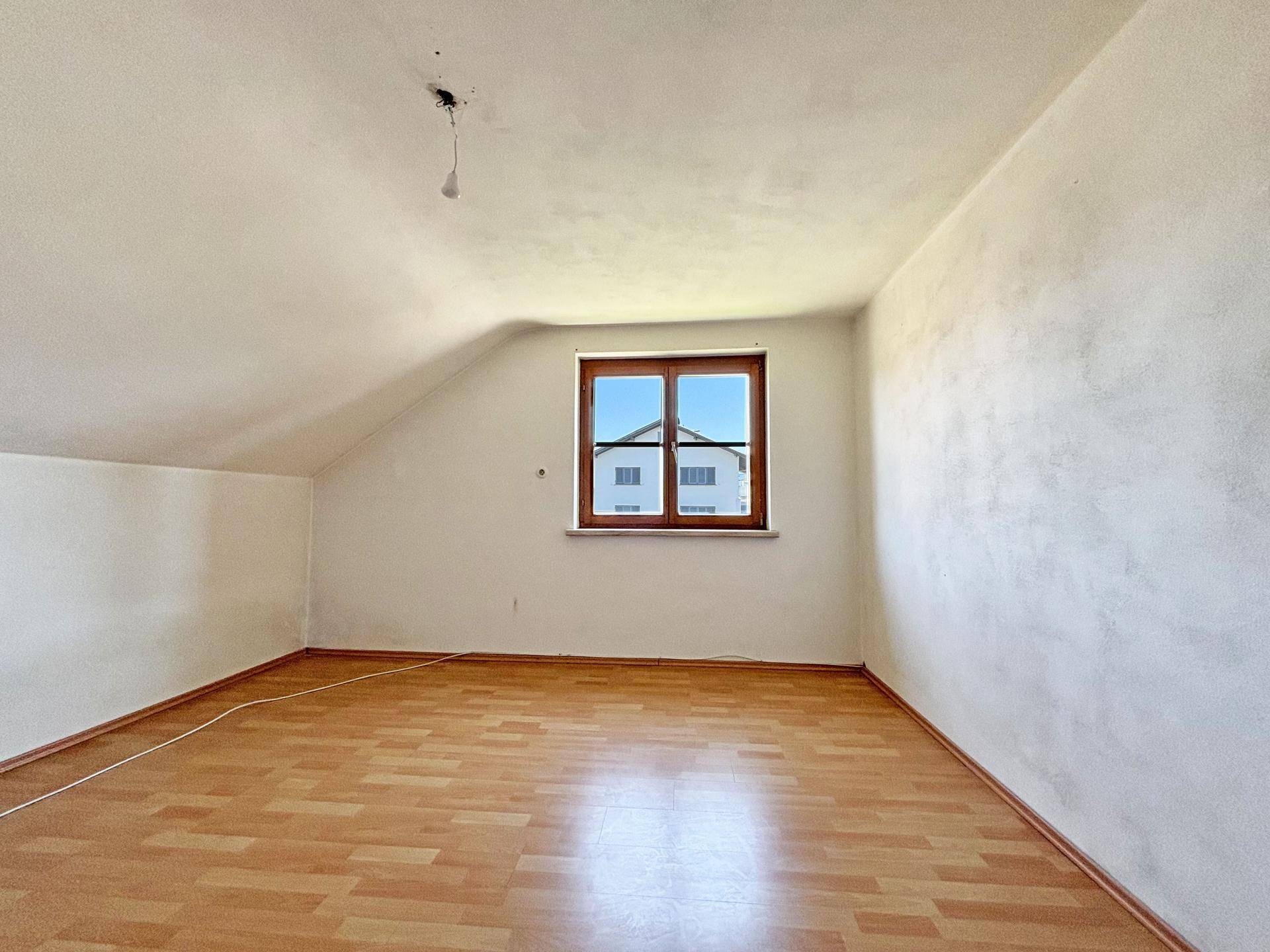 Helles Dachgeschosszimmer mit Laminatboden und schrägen Wänden, ideal als Schlaf- oder Kinderzimmer.