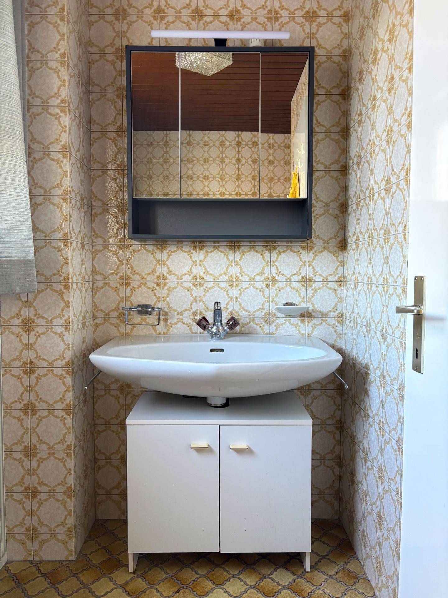 Badezimmer mit gemusterten Fliesen, einem Waschbecken mit Unterschrank und einem Spiegelschrank.