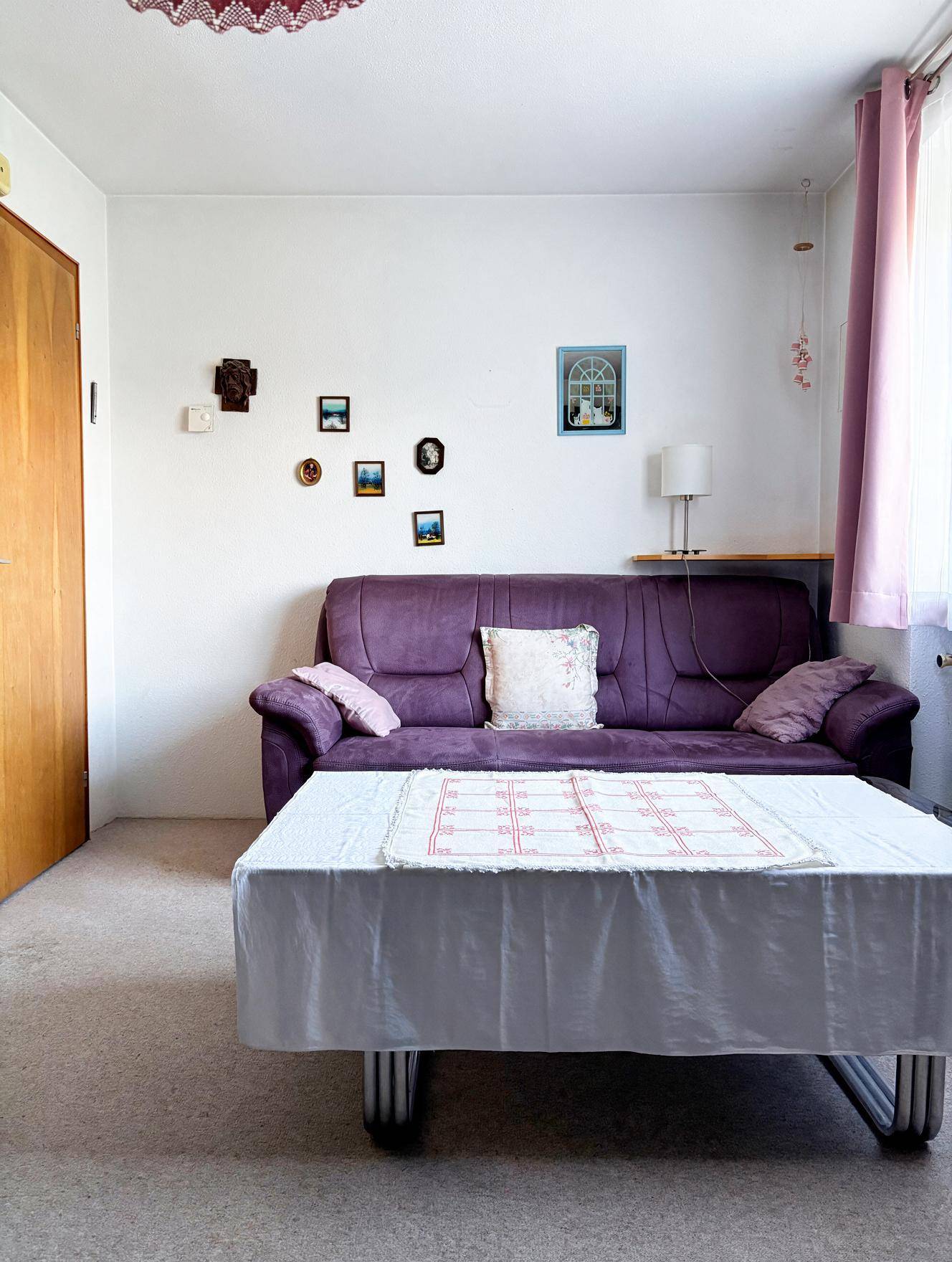 Gemütliches Wohnzimmer mit lila Sofa, Couchtisch und heller Einrichtung, ideal zum Entspannen.