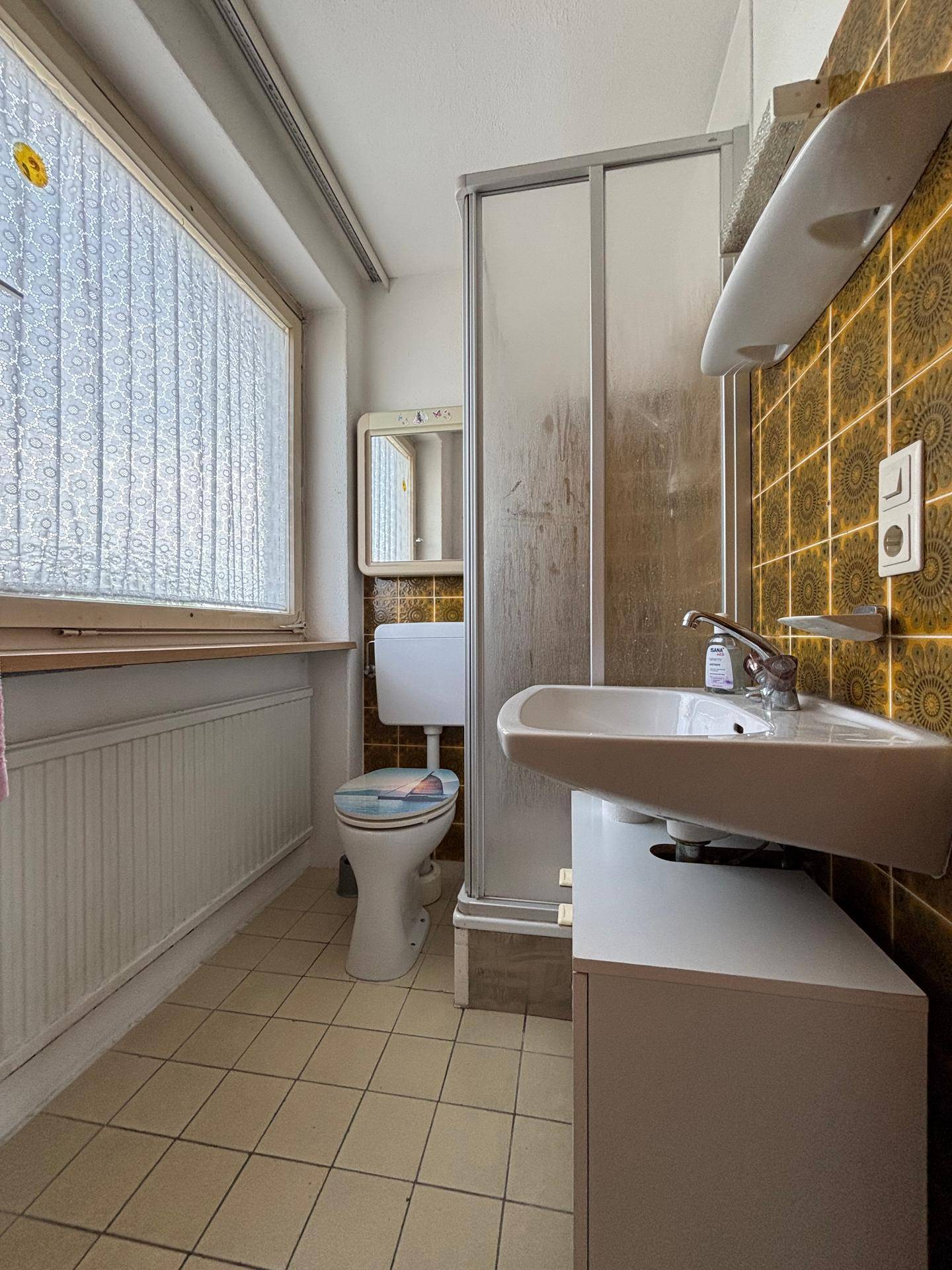 Badezimmer mit Duschkabine, Toilette und einem Fenster, das für natürliche Belüftung sorgt.