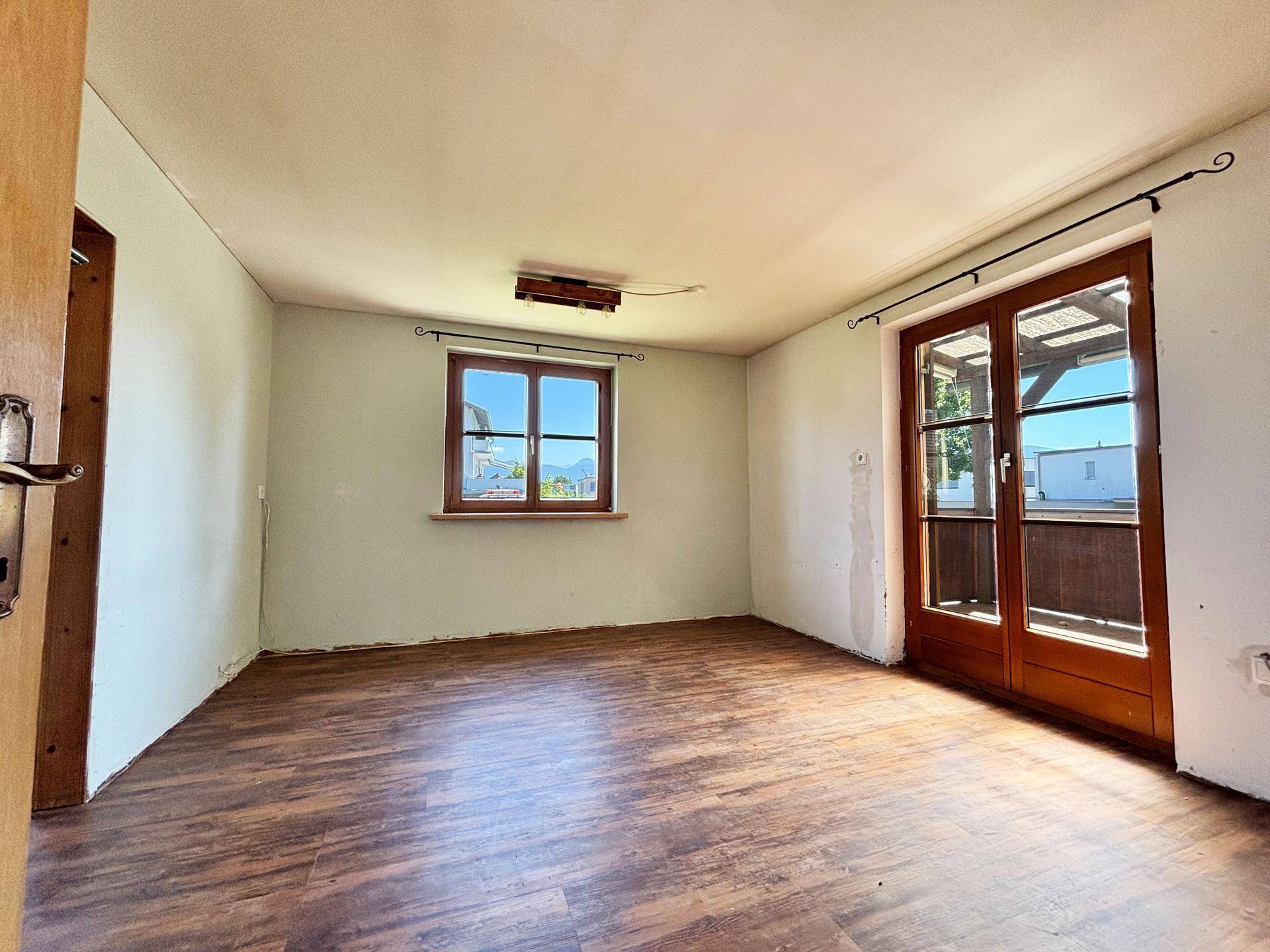 Geräumiger Raum mit Laminatboden und Zugang zu einem Balkon durch eine große Glastür.