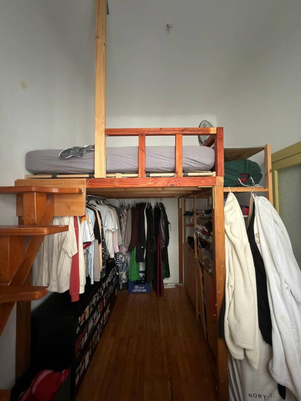 Schlafbereich auf einer Holzempore über einem begehbaren Kleiderschrank mit Holzboden.