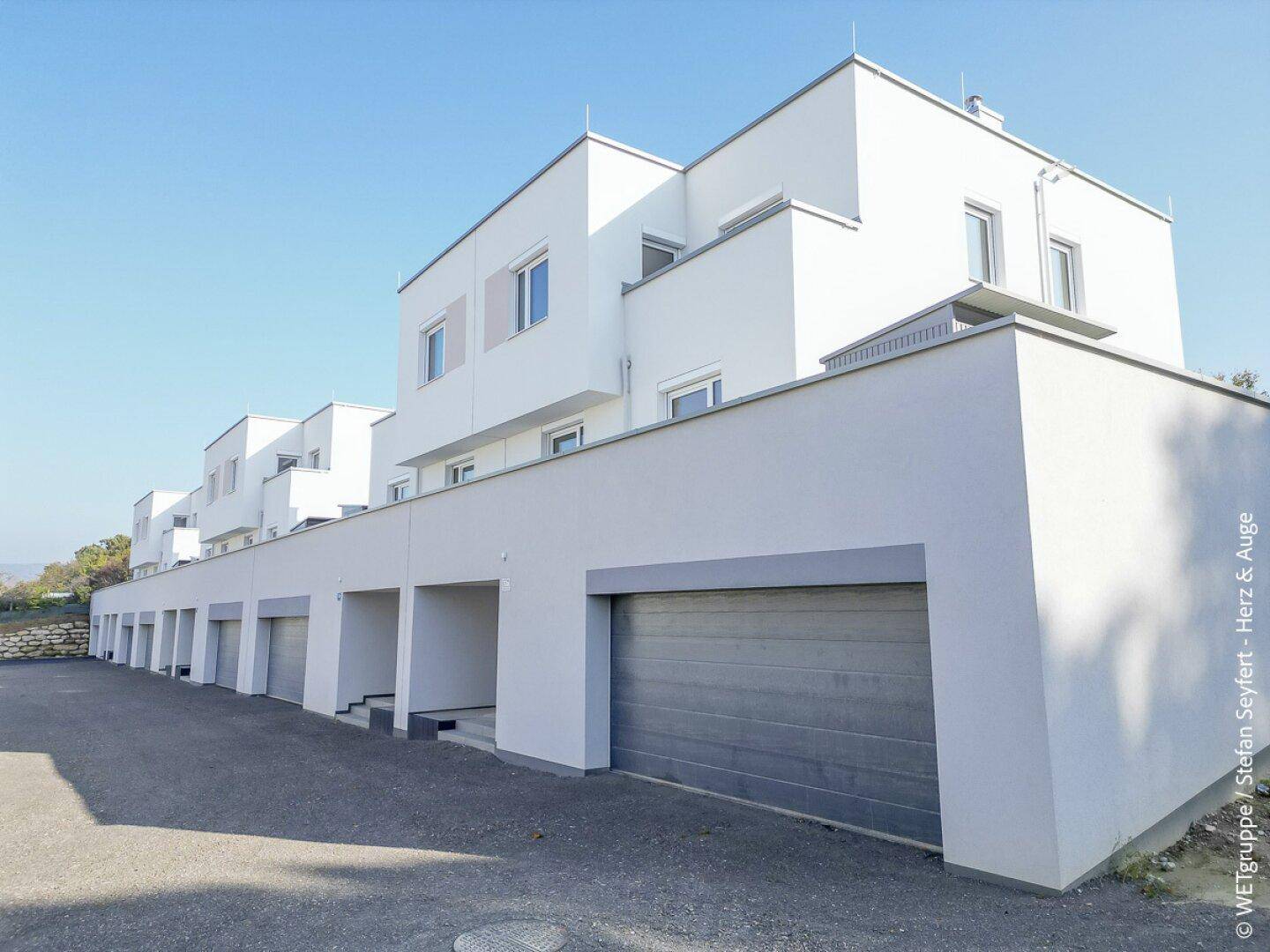 Reihenhausanlage mit integrierten Garagen und modernen Fassaden unter klarem Himmel.
